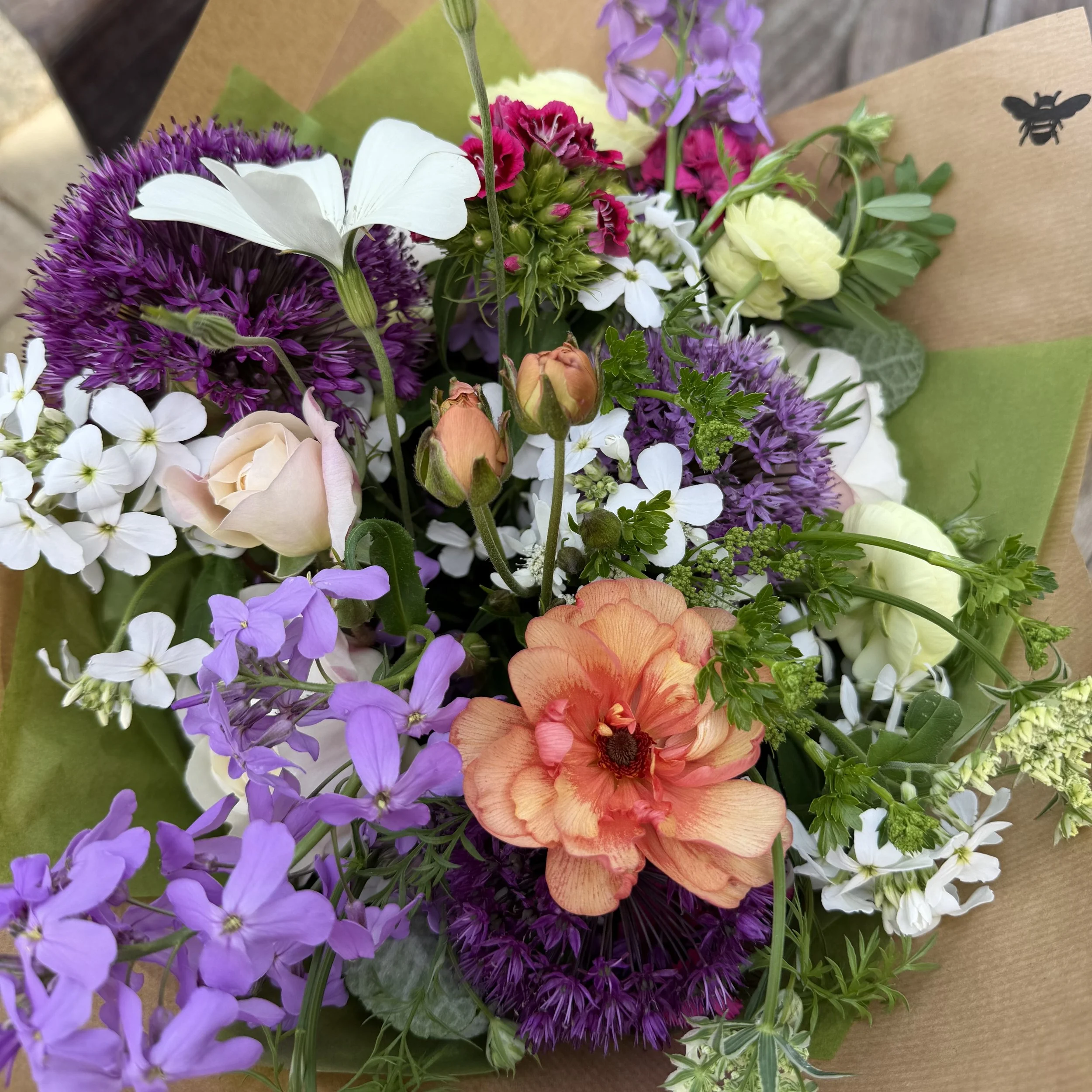 Close-up of a colorful bouquet of various flowers including white butterflies, purple, pink, orange, and white blooms wrapped in brown paper.
