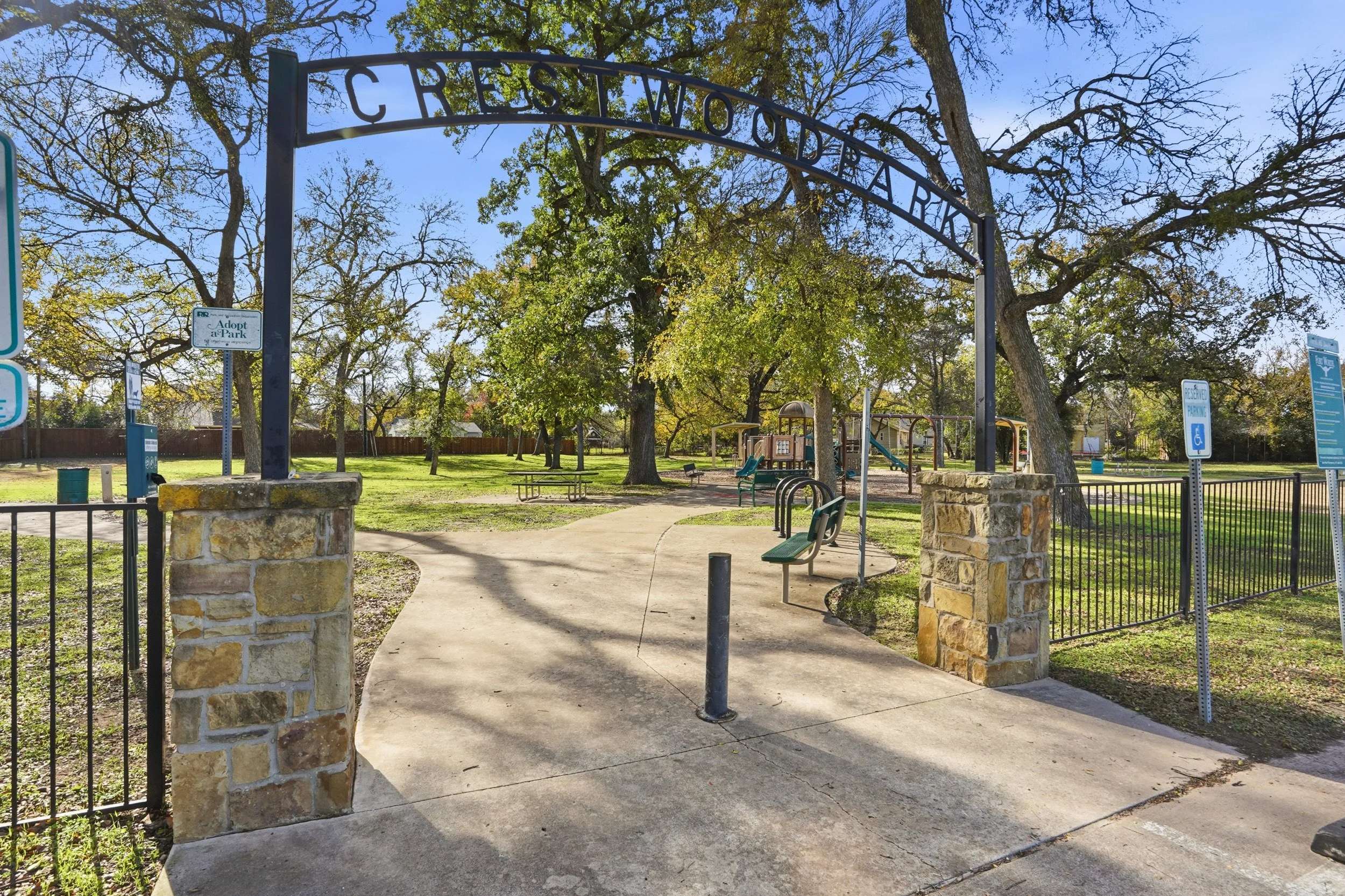 Entrance to Crestwood Park with an archway sign, trees, pathways, benches, and playground equipment, under a sunny sky.