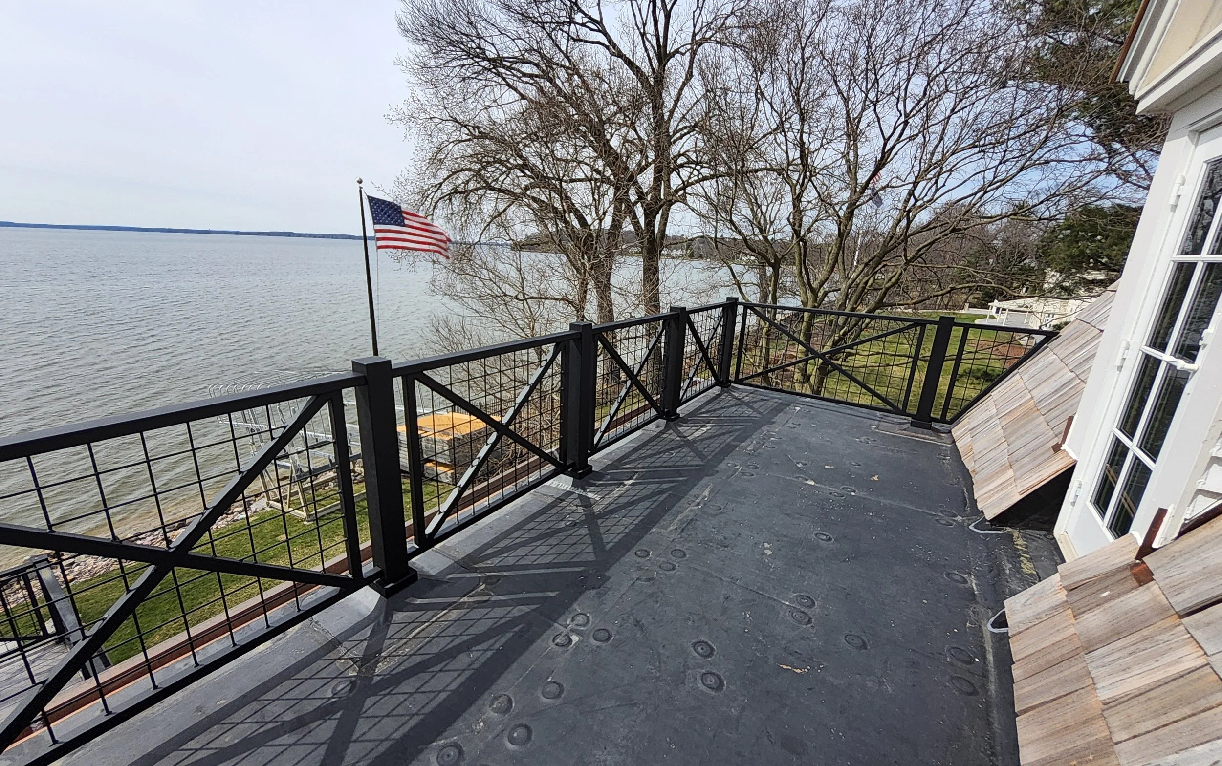 Custom black metal deck railing with a nautical-inspired crossbuck and wire grid design, built by Red Iron Studio for a lakeside rooftop deck. This durable outdoor railing offers unobstructed lake views while adding a classic, coastal-style architect