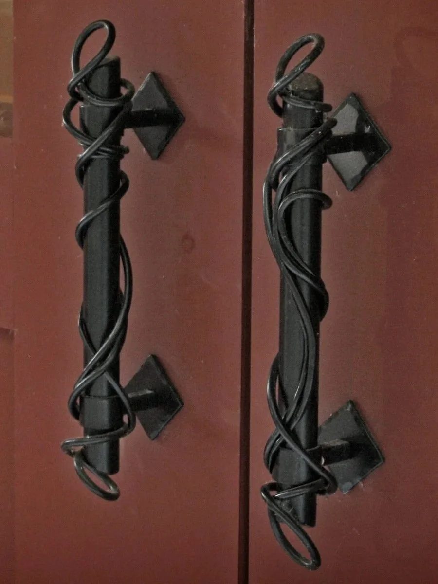 These custom hand-forged iron door pulls feature an artistic twisting vine design wrapped around a sleek center bar, adding organic, handcrafted character to entry doors. A refined blend of form and function, these decorative door handles showcase th
