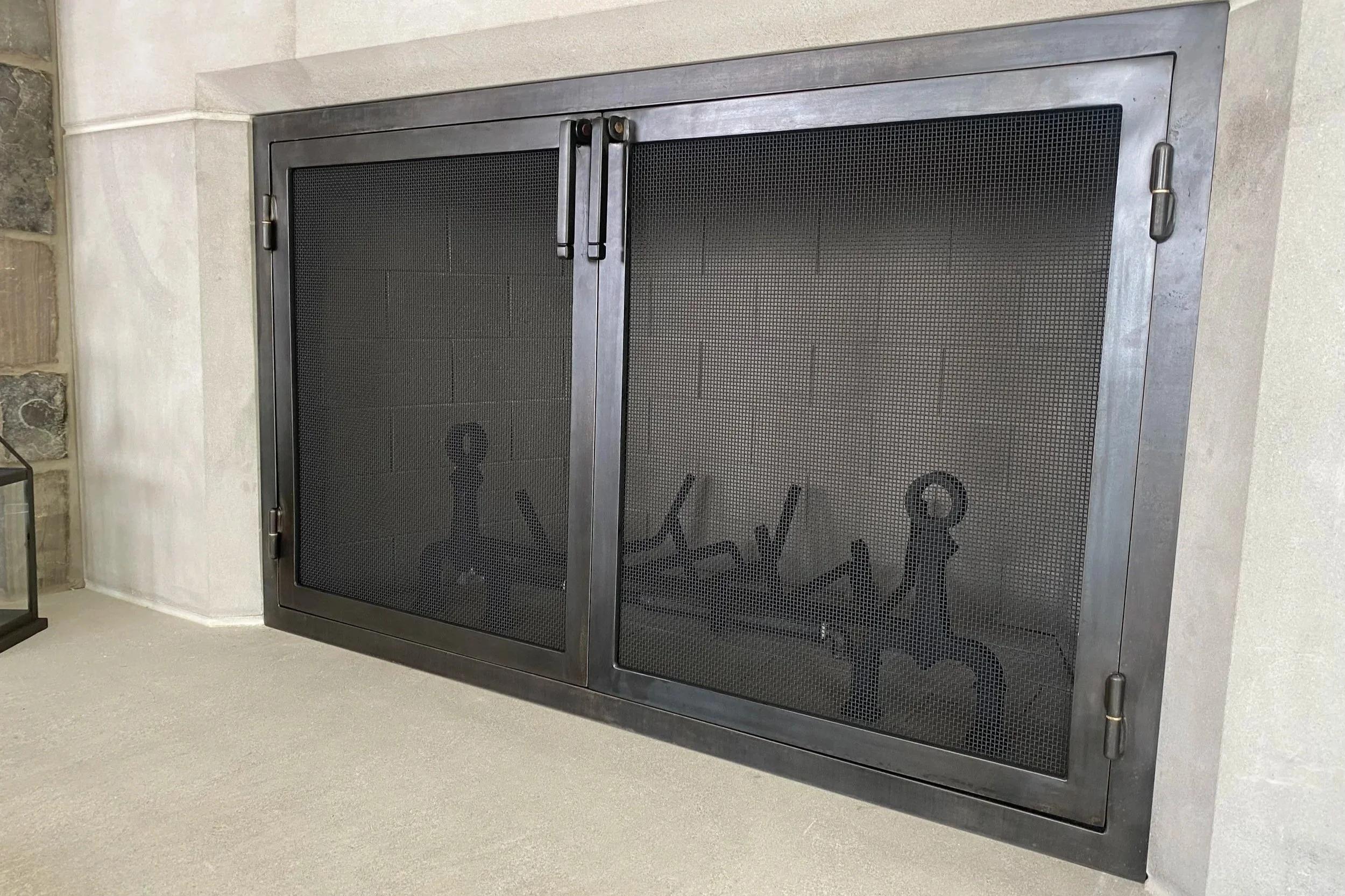 Handcrafted fireplace screen doors by Red Iron Studio, hand-forged in blackened steel with a clean square frame and fine mesh panels to fit a modern concrete hearth. This handcrafted fire screen delivers sleek, contemporary iron craftsmanship for a m