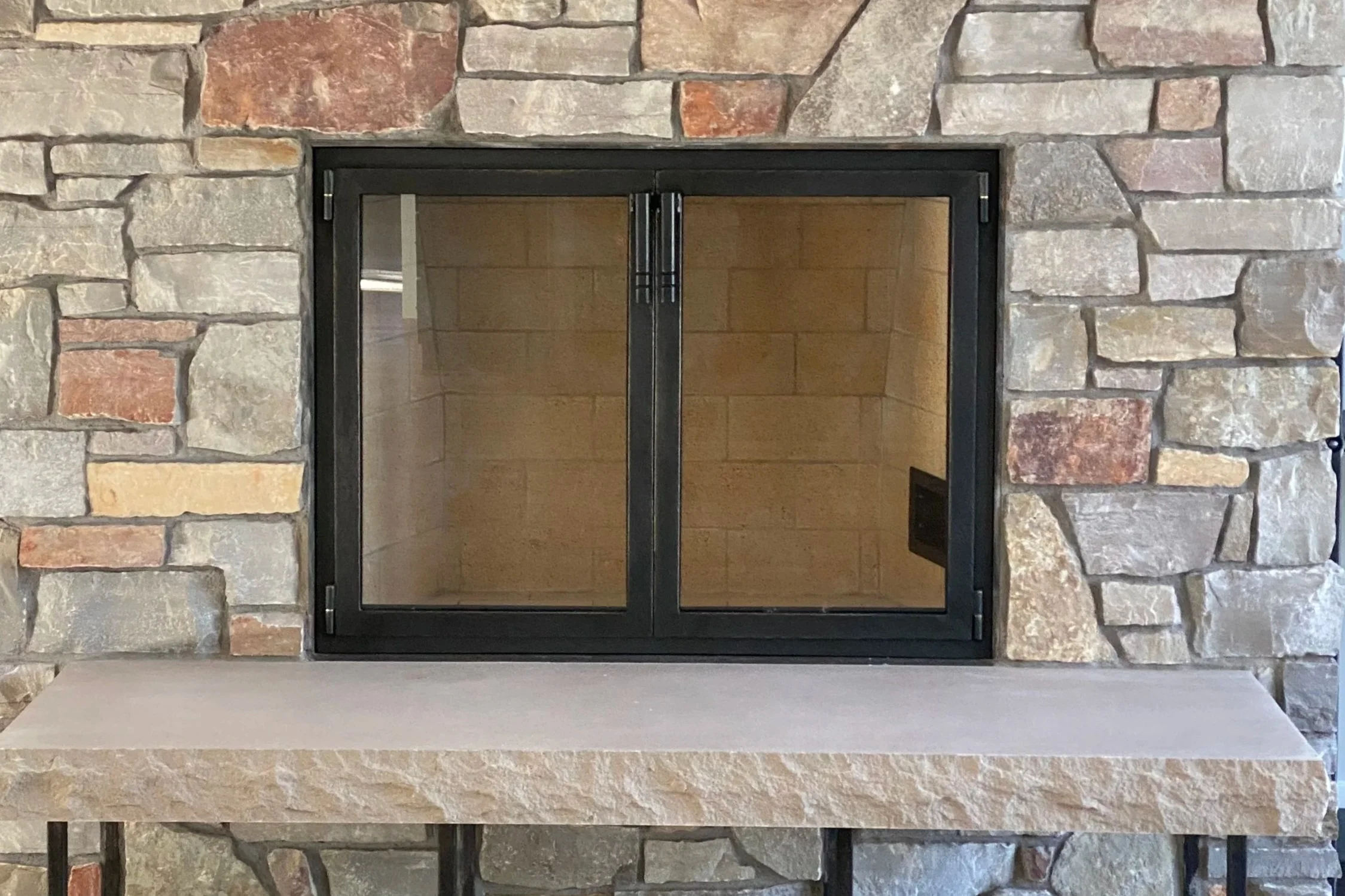 Custom minimalist fireplace doors by Red Iron Studio, hand-forged in sleek black steel with clean square lines to complement a modern stacked-stone hearth and matching iron hearth bench. These handcrafted iron fireplace doors offer a contemporary, in