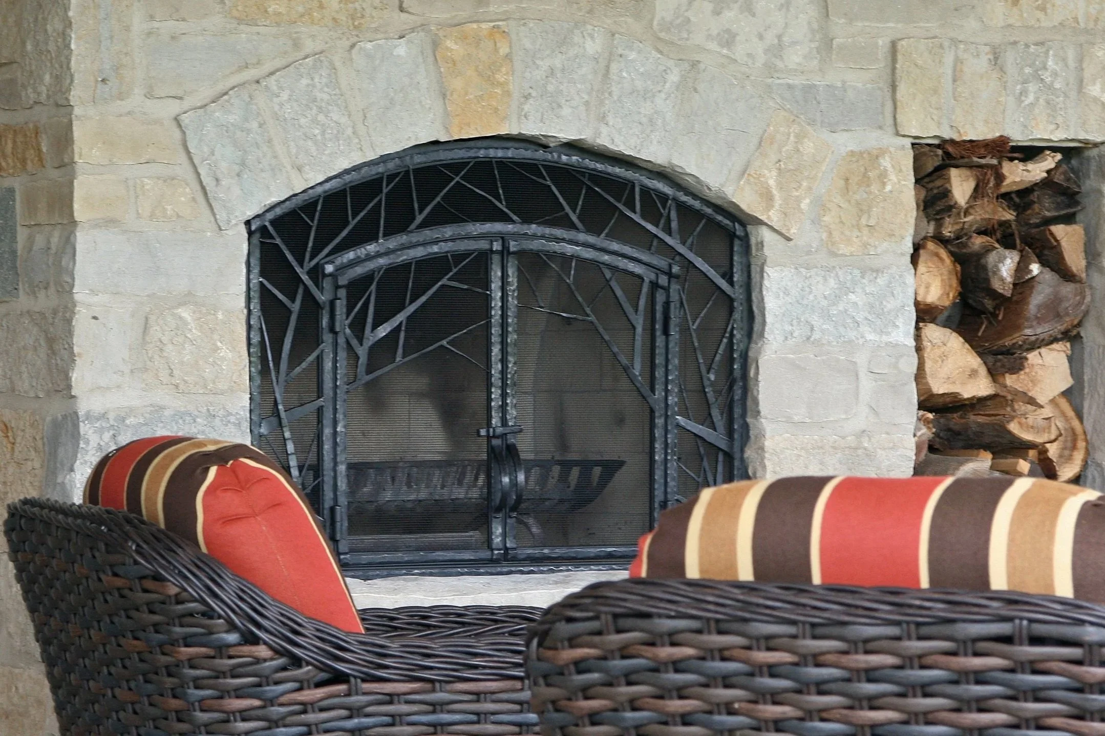 Custom hand-forged fireplace screen by Red Iron Studio, featuring an organic branch-and-twig arched design in blackened iron, built to fit a stone outdoor fireplace. This rustic-modern fire screen blends natural, woodland-inspired ironwork with funct