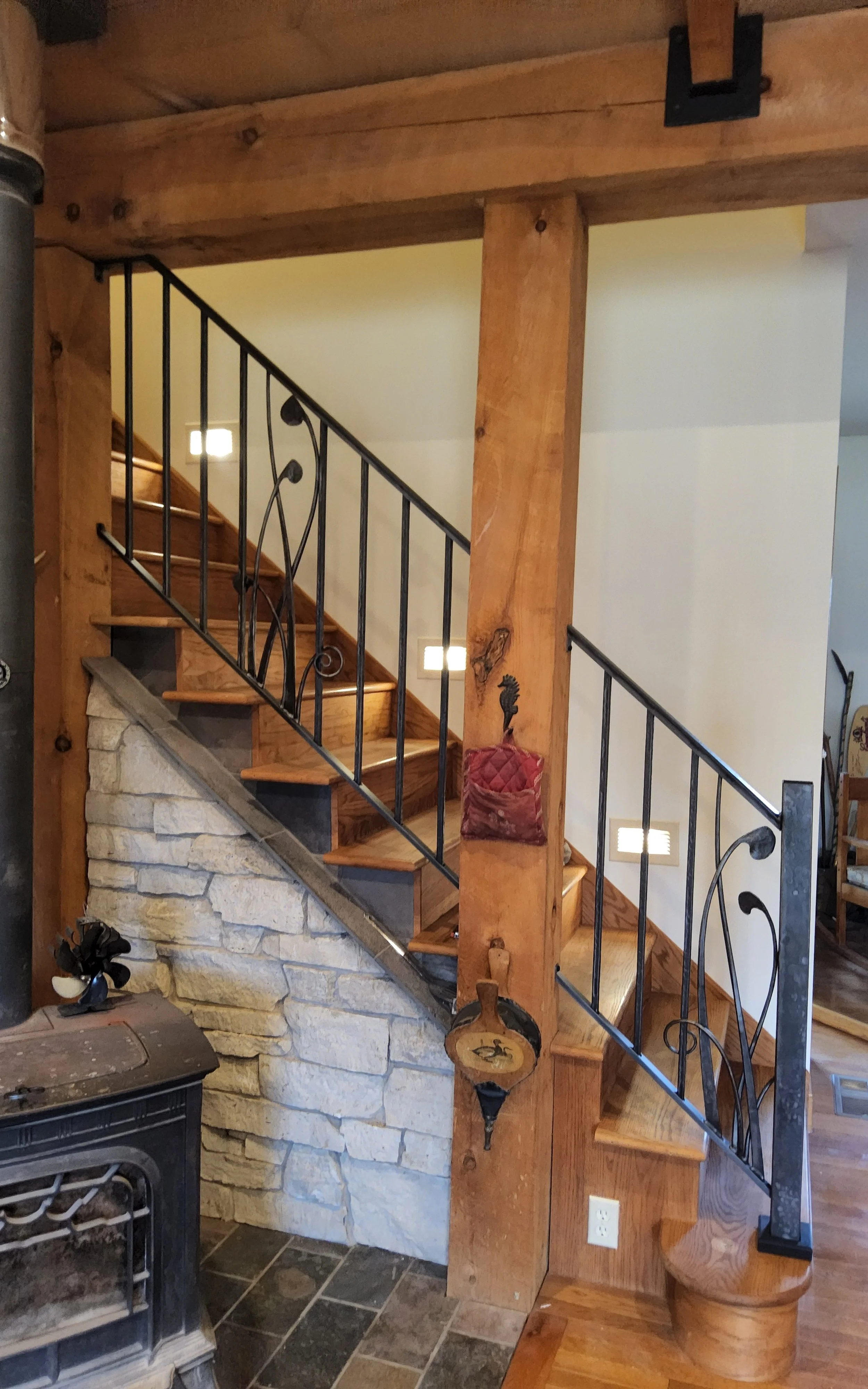 Hand-forged wrought iron stair railing with organic scrolled leaf and vine details, custom-built by Red Iron Studio for a rustic timber-frame home. This artisan ironwork railing brings a nature-inspired, hand-crafted touch to the wood beams and stone