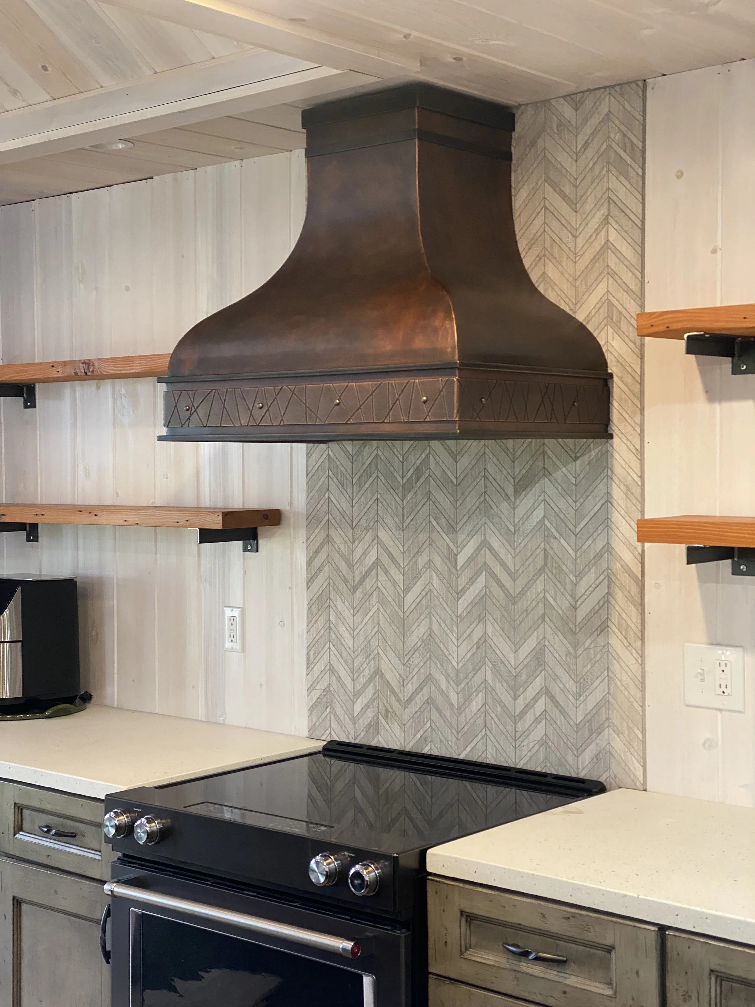 Handcrafted Copper Range Hood with Hand-Hammered Detailing - This custom copper range hood features a rich, hand-patinated finish and intricate hand-tooled banding, adding warm, artisanal character to a rustic farmhouse kitchen. A statement piece of 
