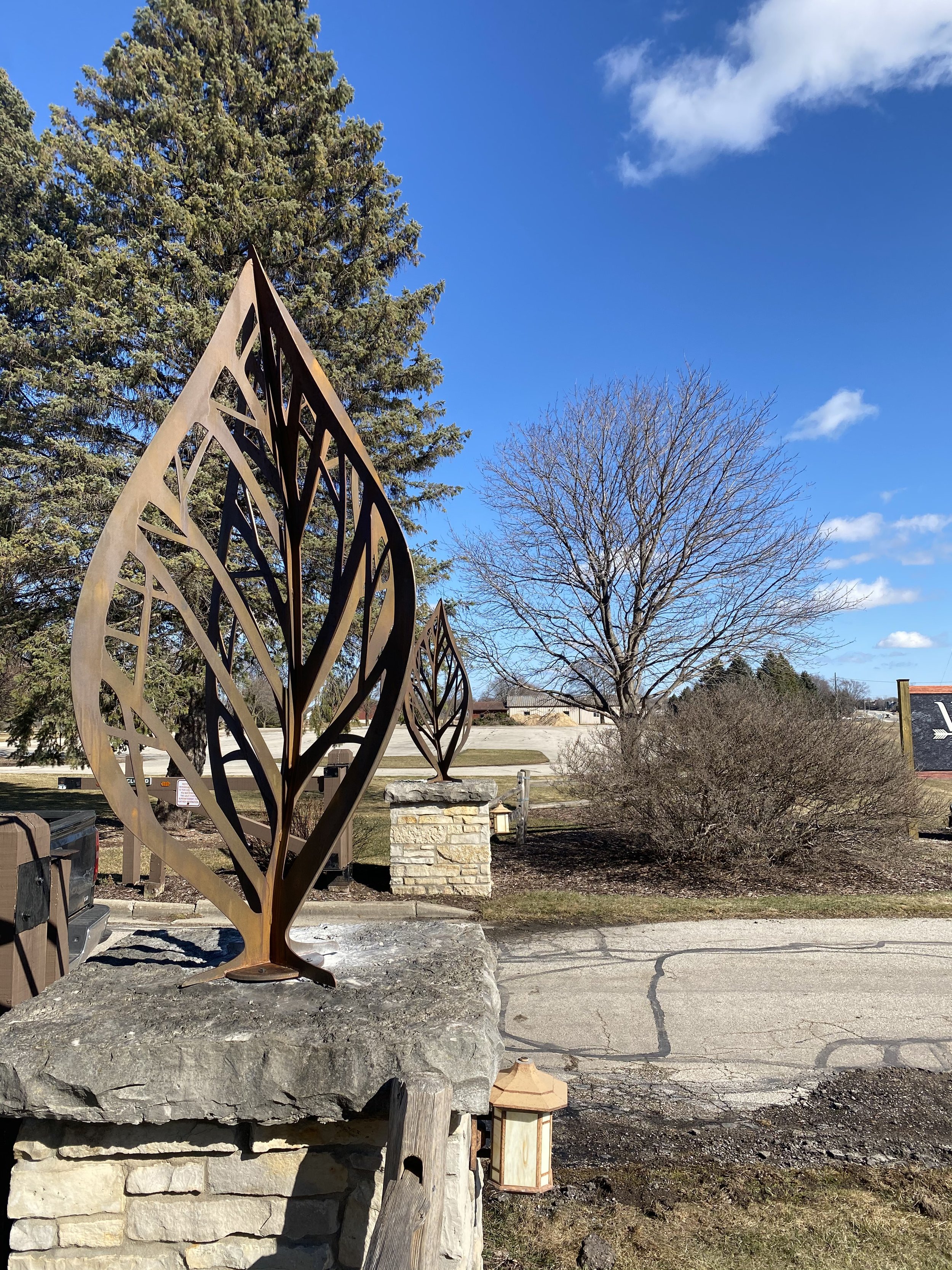 Corten Steel Leaf Sculptures – Custom Metal Gate Entrance Accents - These hand-forged corten steel leaf sculptures showcase intricate laser-cut vein detailing and a rich natural rust patina, mounted atop stone gate pillars for a striking entrance sta