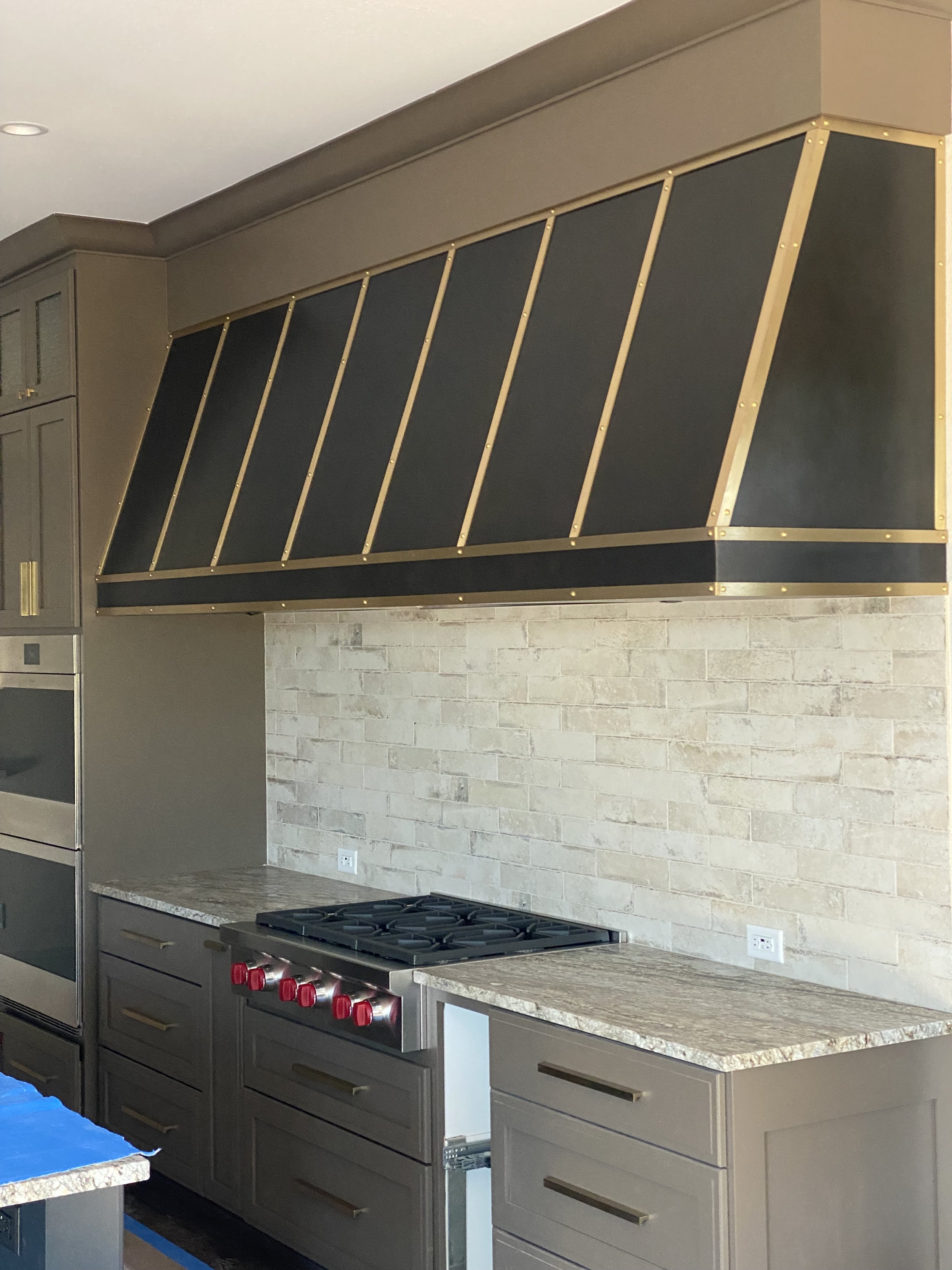 Custom Blackened Steel Range Hood with Brass Strapping & Rivet Detail - This bold, angular range hood features hand-applied brass strapping and riveted seams over a blackened steel finish, delivering an industrial-luxe focal point for a professional-