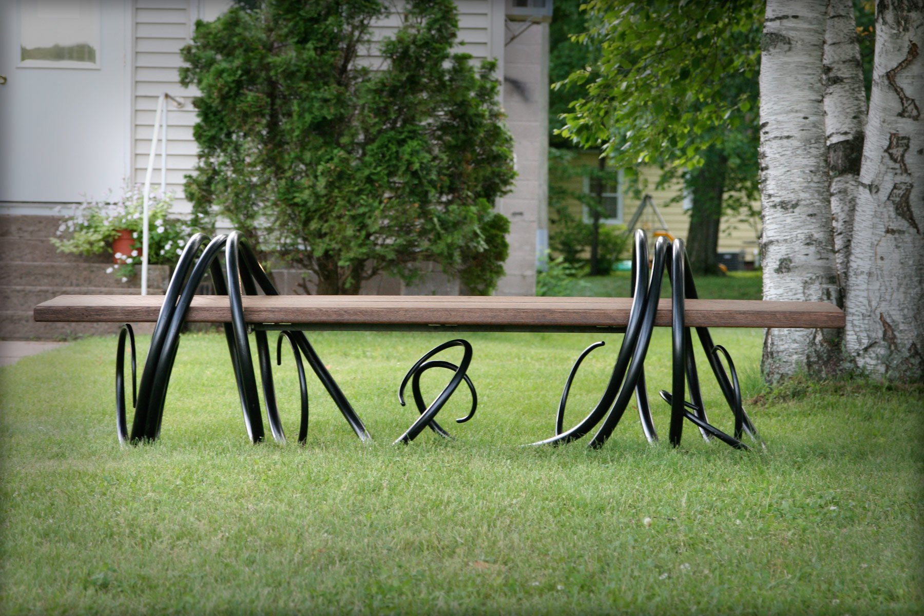 This one-of-a-kind outdoor bench features a solid wood seat supported by playful, hand-forged curling iron legs, blending organic sculptural design with functional seating for gardens and patios. A whimsical statement piece for outdoor living spaces,