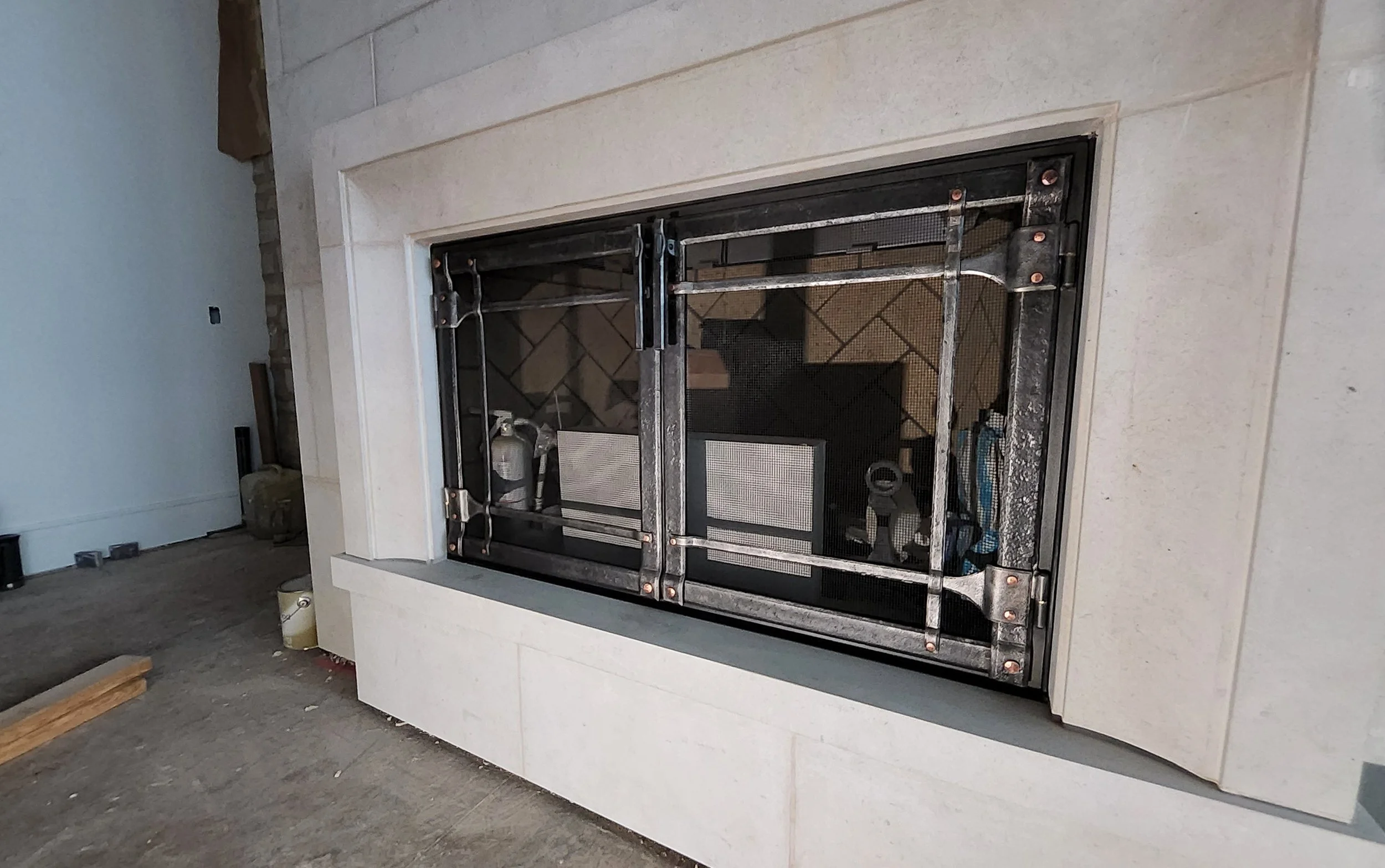 Custom hand-forged fireplace screen by Red Iron Studio, featuring a bold iron frame with copper rivet details and fine mesh panels, fitted to a honed stone fireplace surround. This handcrafted fire screen pairs sturdy blacksmith construction with cle
