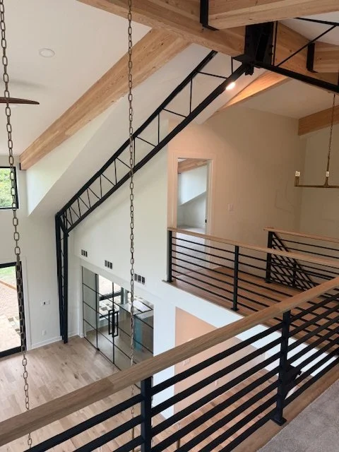 Modern black steel horizontal bar railing with wood cap rail by Red Iron Studio, installed along an open loft landing beneath exposed black steel stair stringers in a bright, vaulted-ceiling home.
