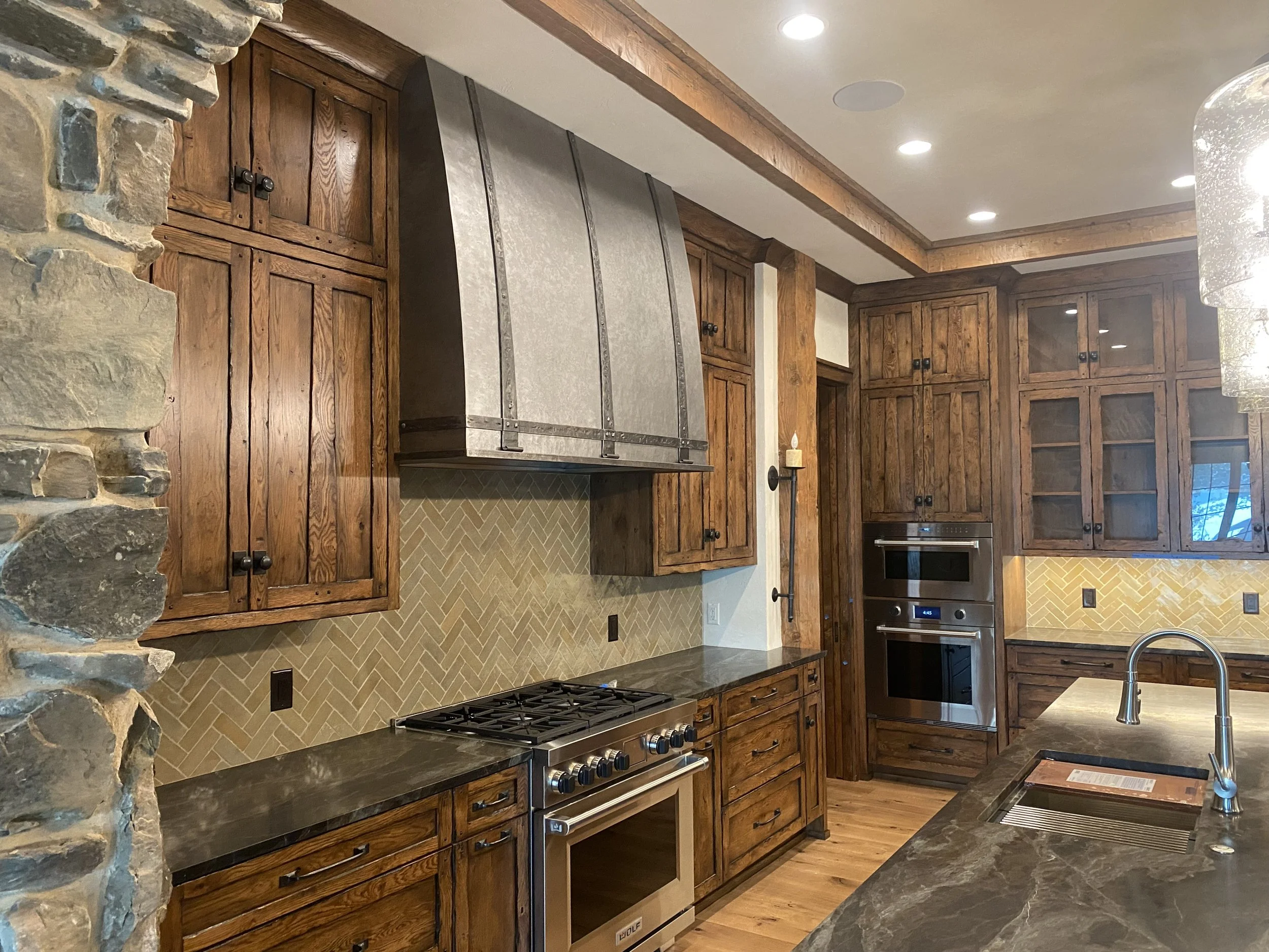 Custom Galvanized Steel Range Hood with Hand-Forged Iron Straps -This curved, hand-hammered galvanized steel range hood is accented with rustic wrought iron banding and rivets, creating a warm mountain-lodge focal point above a Wolf range. Custom-bui