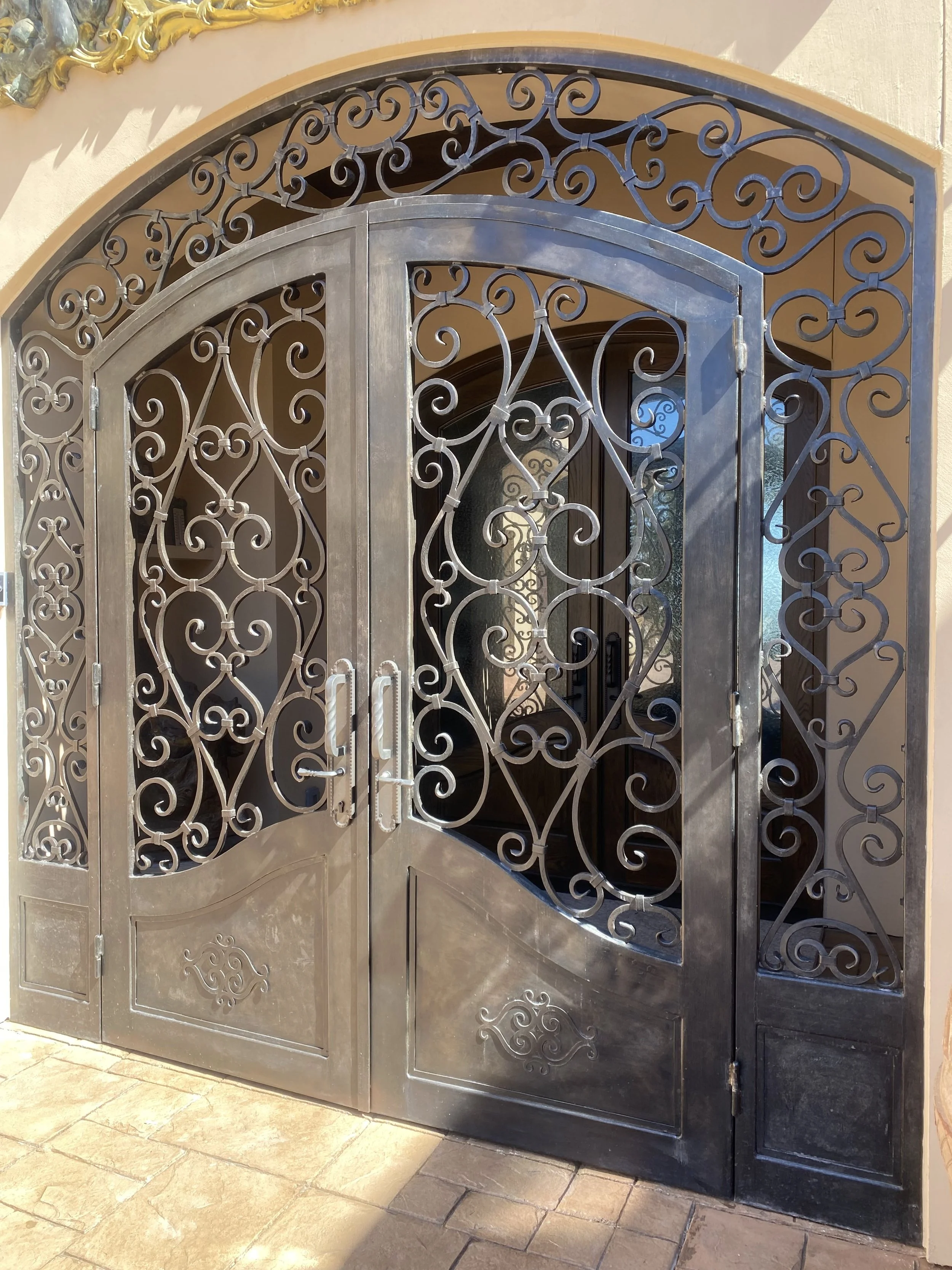 Custom Wrought Iron Double Entry Doors with Arched Transom - This grand custom wrought iron entry door system features ornate scrollwork, an arched glass transom, and matching sidelights for a dramatic, Old World-inspired entrance. Handcrafted for lu