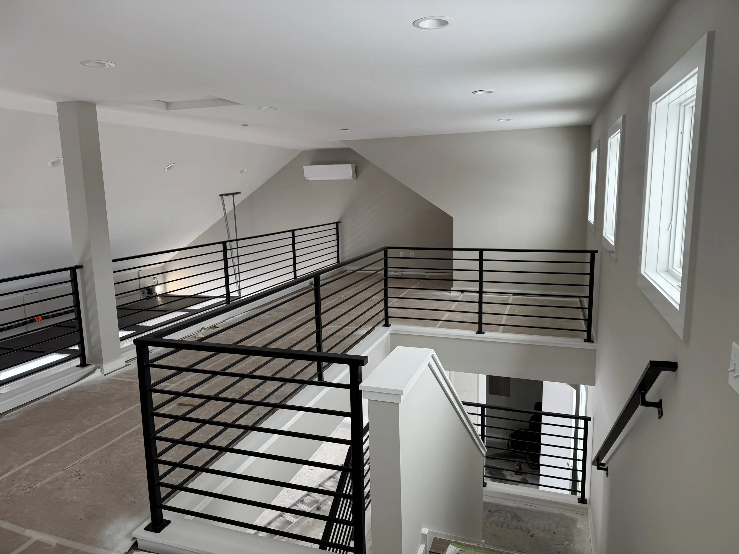 Modern black steel horizontal bar railing by Red Iron Studio, installed along an open loft landing and staircase in a minimalist, under-construction multi-level home.