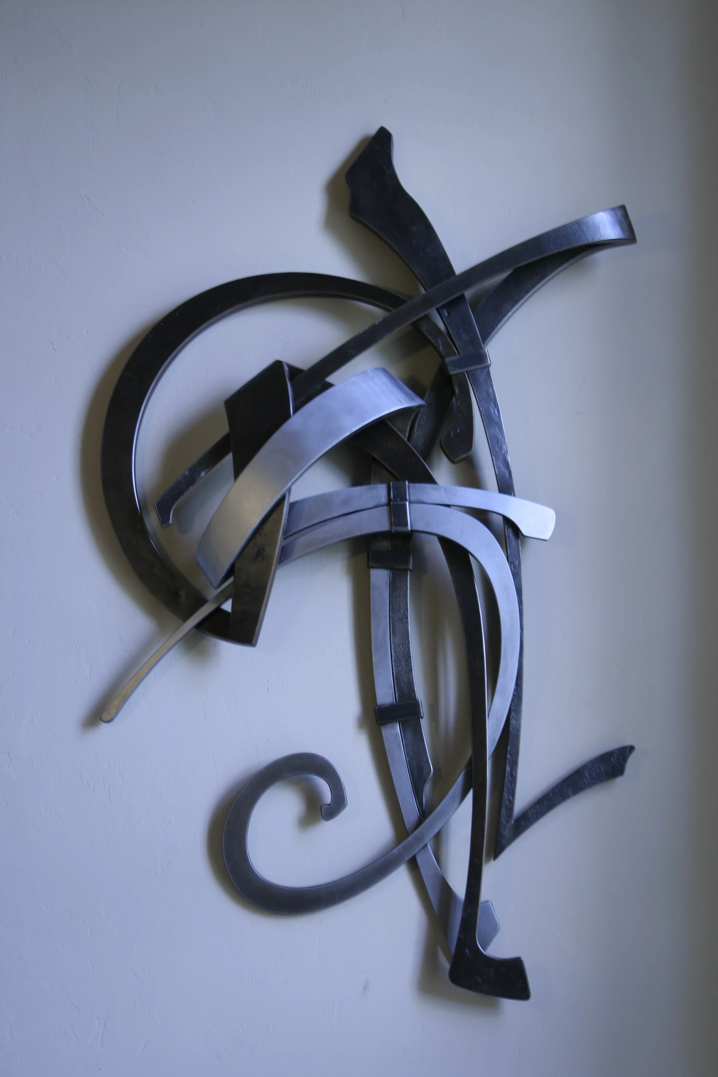 Handcrafted Steel Range Hood – Abstract Forged Metal Sculpture - This custom hand-forged steel range hood combines sweeping, calligraphic ribbons of blackened and brushed steel into a bold, sculptural kitchen focal point. A striking example of artisa