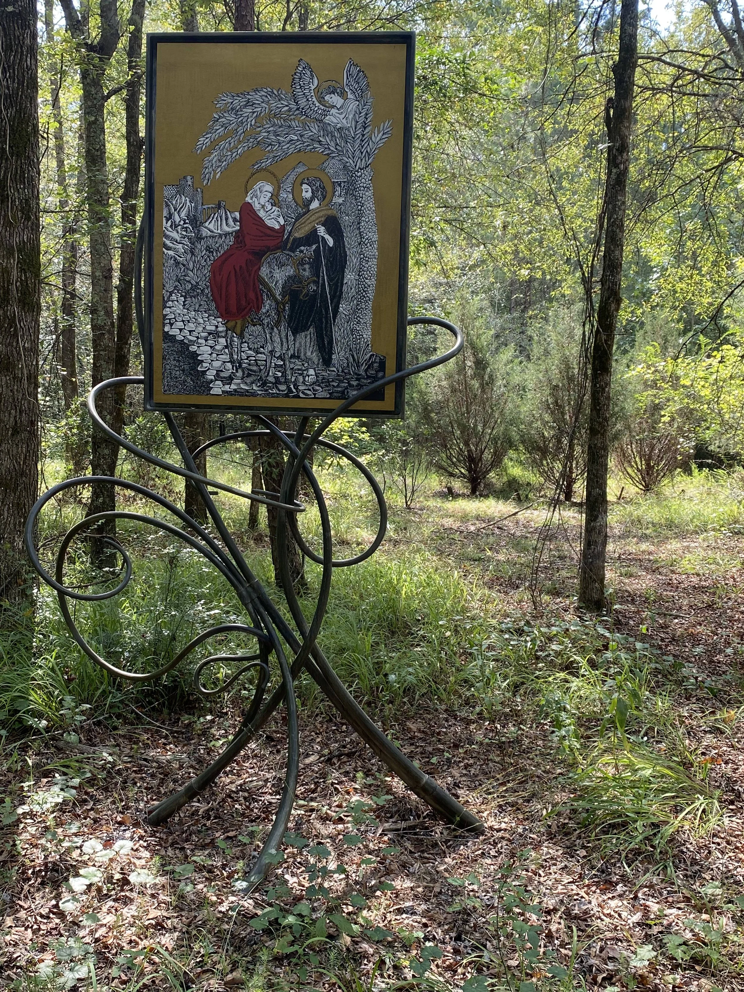 Hand-Forged Iron Easel Stand with Religious Icon Painting - This custom hand-forged iron easel stand features flowing, sculptural scrollwork legs supporting a devotional religious icon painting of the Holy Family, designed for outdoor prayer gardens,