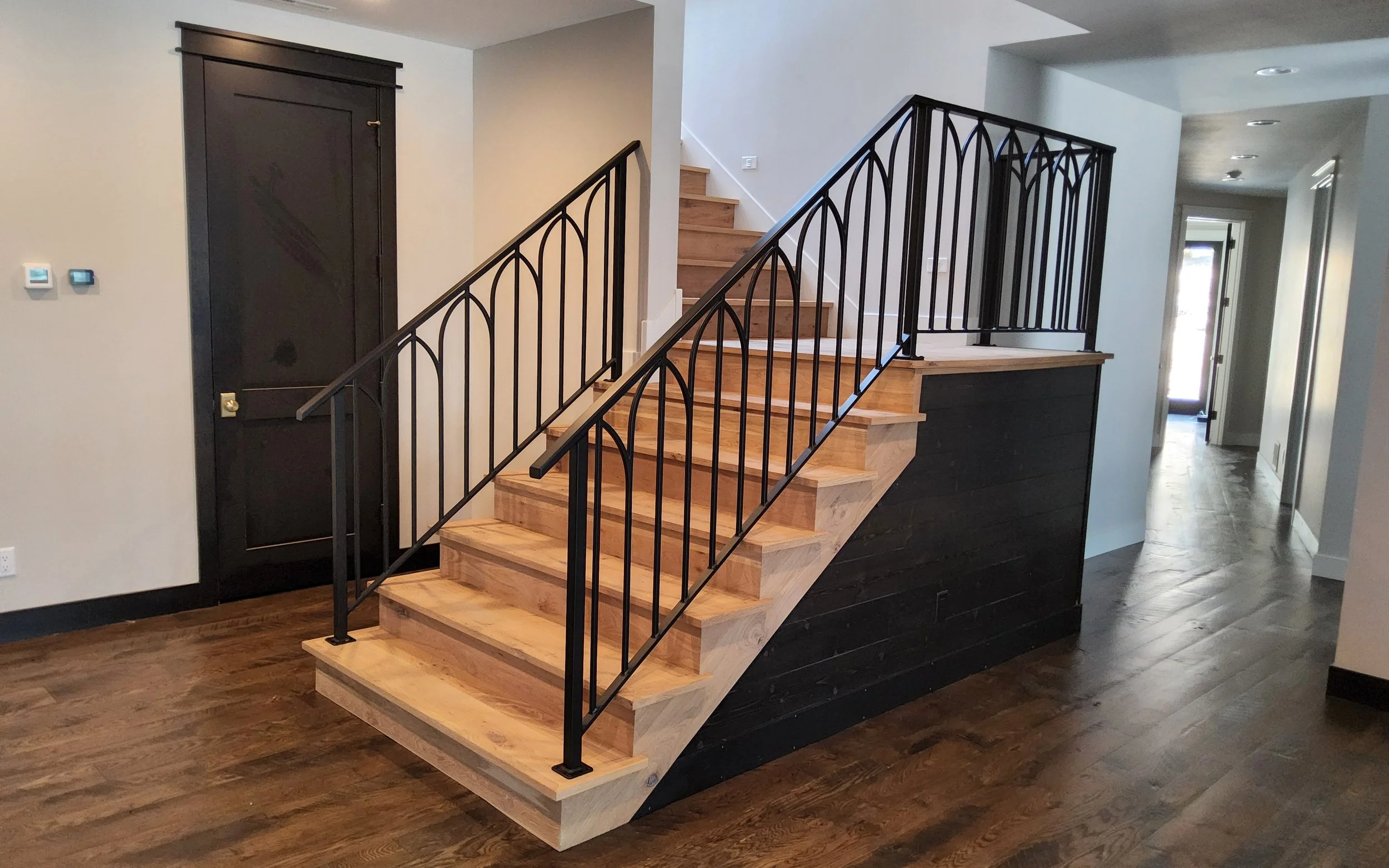 Custom black wrought iron stair railing with an arched picket design by Red Iron Studio, installed on a modern staircase with natural wood treads and matching landing rail. This handcrafted iron railing combines gothic-inspired arches with a contempo
