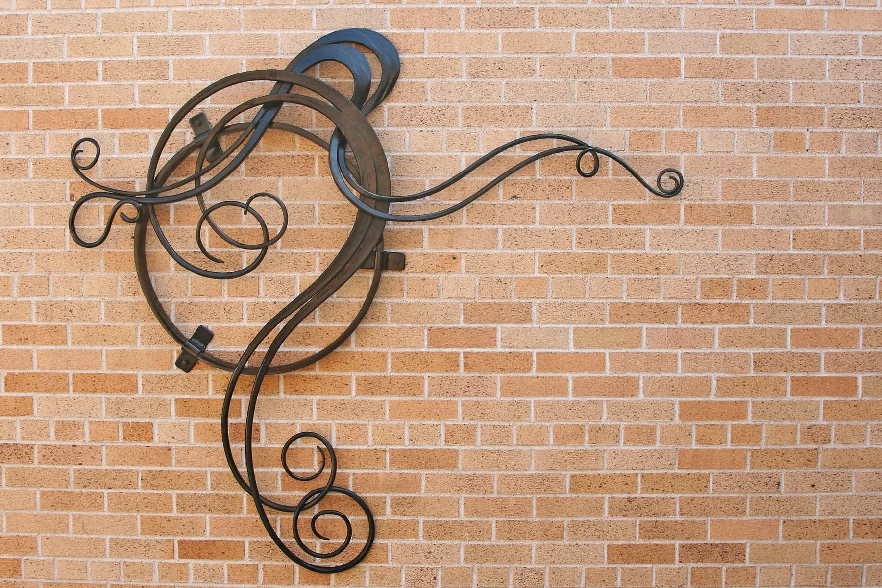 This large-scale hand-forged steel wall sculpture features intertwining circular forms and delicate scrollwork spirals, creating an elegant architectural focal point for medical facilities and commercial buildings. Custom-designed for a medical clini