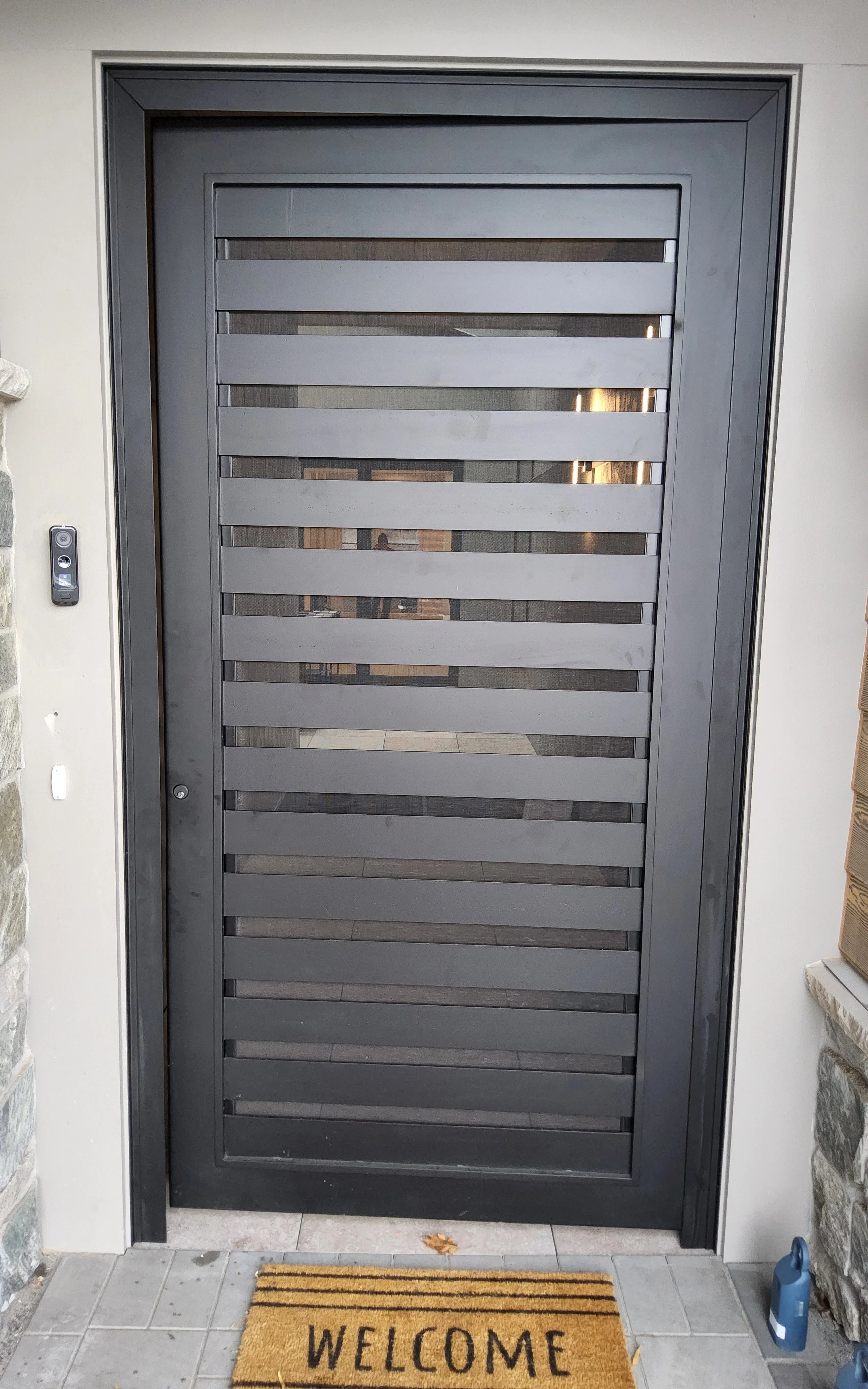 This sleek, custom iron entry door features a contemporary horizontal slat design with privacy glass panels, offering a striking modern aesthetic paired with security and natural light. Ideal for modern and transitional homes, this custom steel door 
