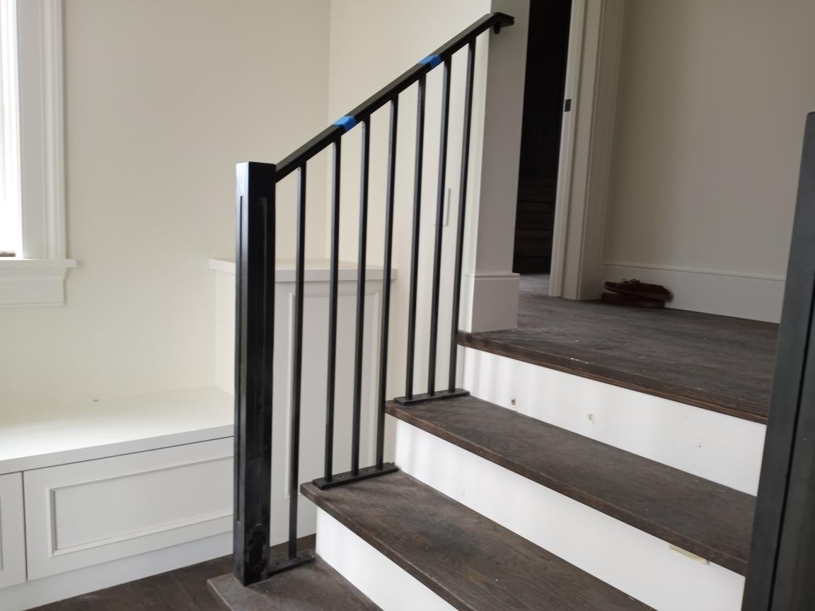 Sleek black steel stair railing with simple square balusters and a substantial squared newel post, custom-fabricated by Red Iron Studio for a transitional interior staircase. This minimalist metal railing pairs a clean, contemporary profile with rich