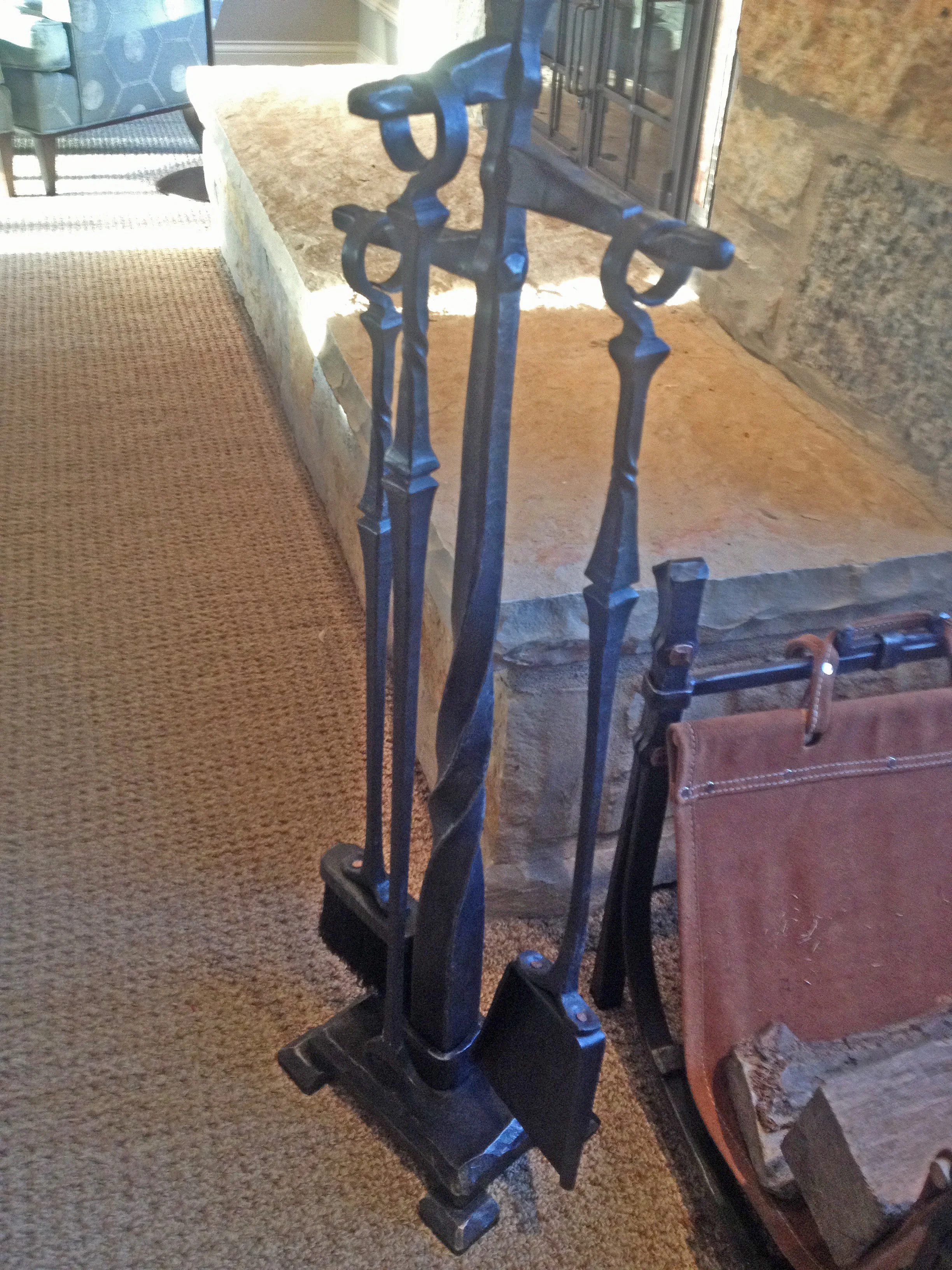Custom hand-forged fireplace tool set by Red Iron Studio, featuring a twisted iron shaft, sculptural ring handles, and a matching stand, paired with a leather log carrier. This handcrafted fireplace accessory set combines fine blacksmithing detail wi