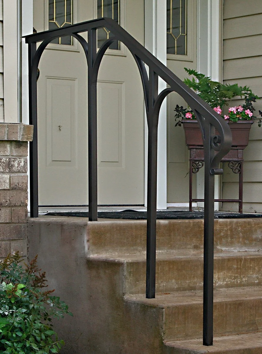 This wrought iron entry railing by Red Iron Studio features graceful arched supports and a subtle scrolled foot, adding an elegant, architectural touch to a classic front porch stoop. Its sculptural silhouette proves a functional handrail can double 