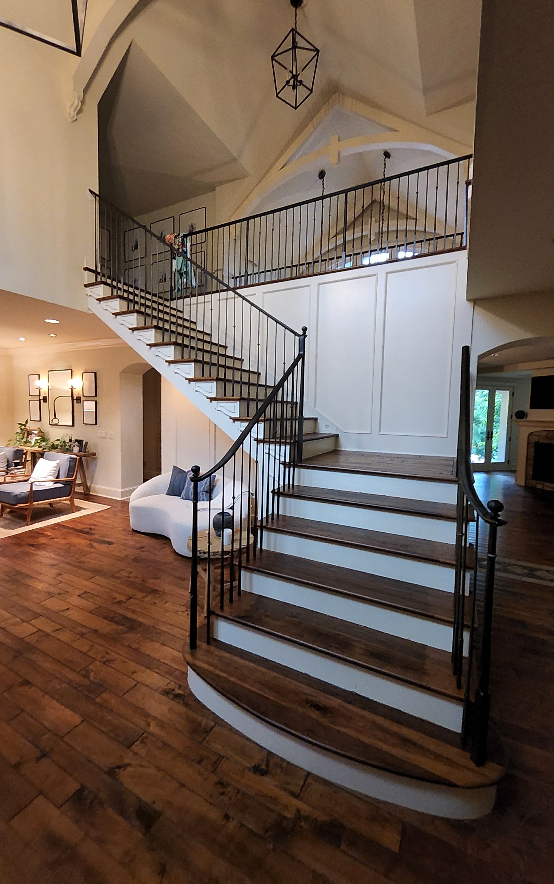 Traditional wrought iron stair railing with a graceful curved handrail and classic twisted balusters, custom-crafted by Red Iron Studio for a grand curved staircase. This elegant iron railing complements the home's vaulted ceilings and rich wood floo