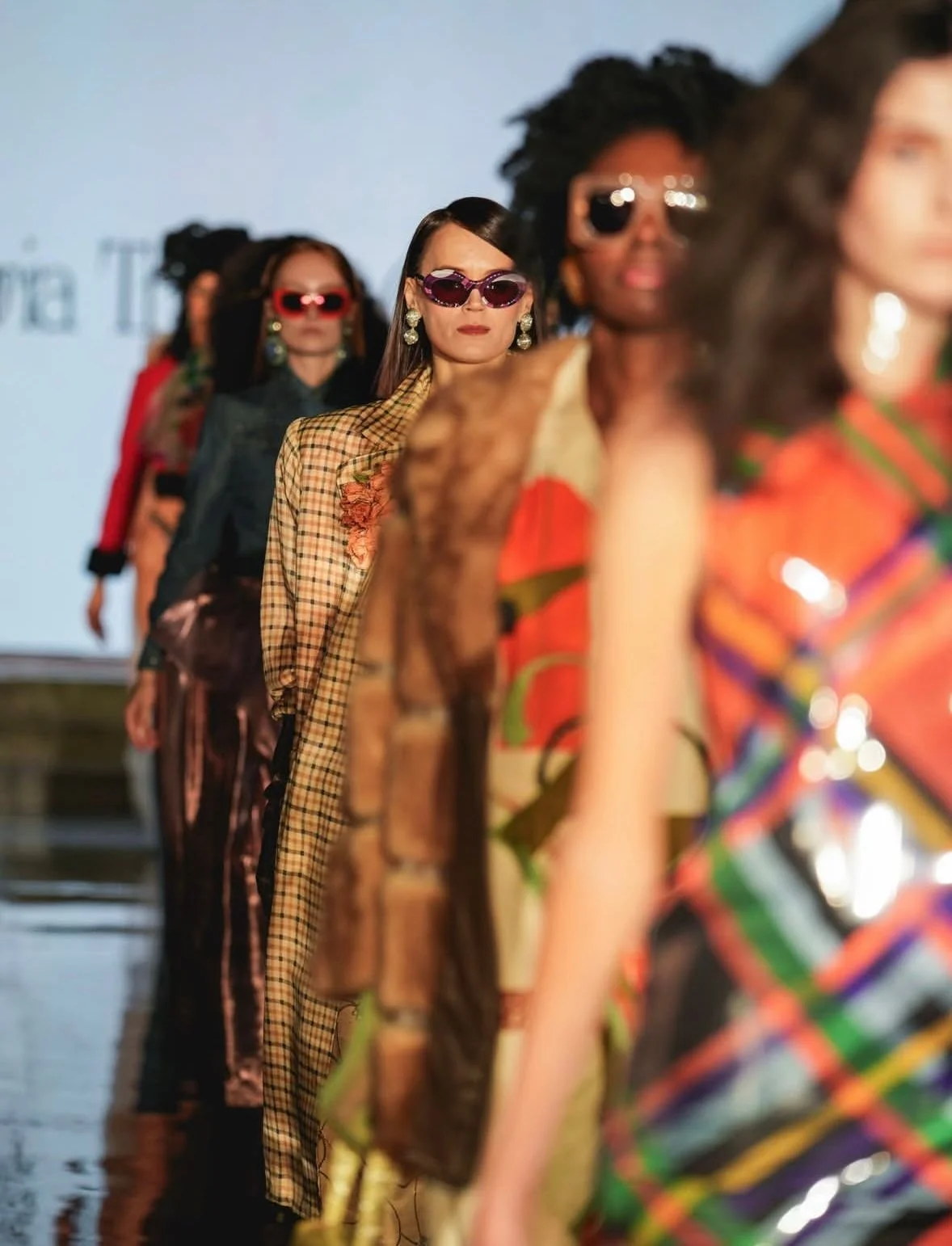 Une rangée de femmes défiler sur une passerelle lors d un défilé de mode, portant des vêtements colorés et des lunettes de soleil.