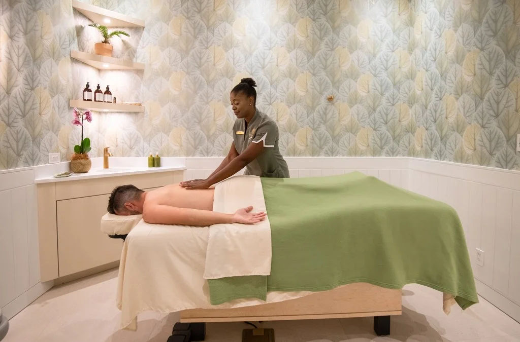 A person receiving a massage in a spa room with a massage therapist standing next to them.