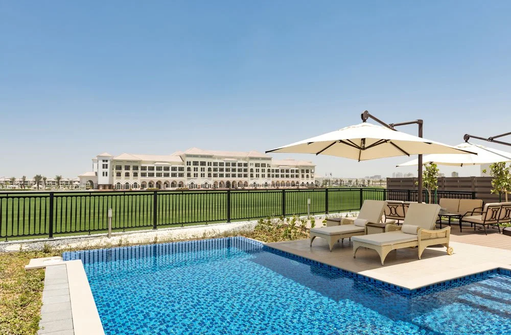 Luxury poolside area with lounge chairs and umbrellas, overlooking a large building in the distance, under clear blue sky.