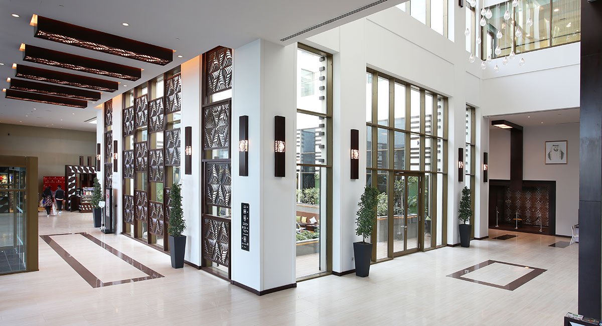 Modern hotel lobby with large windows, decorative wall panels, indoor plants, and stylish lighting fixtures.