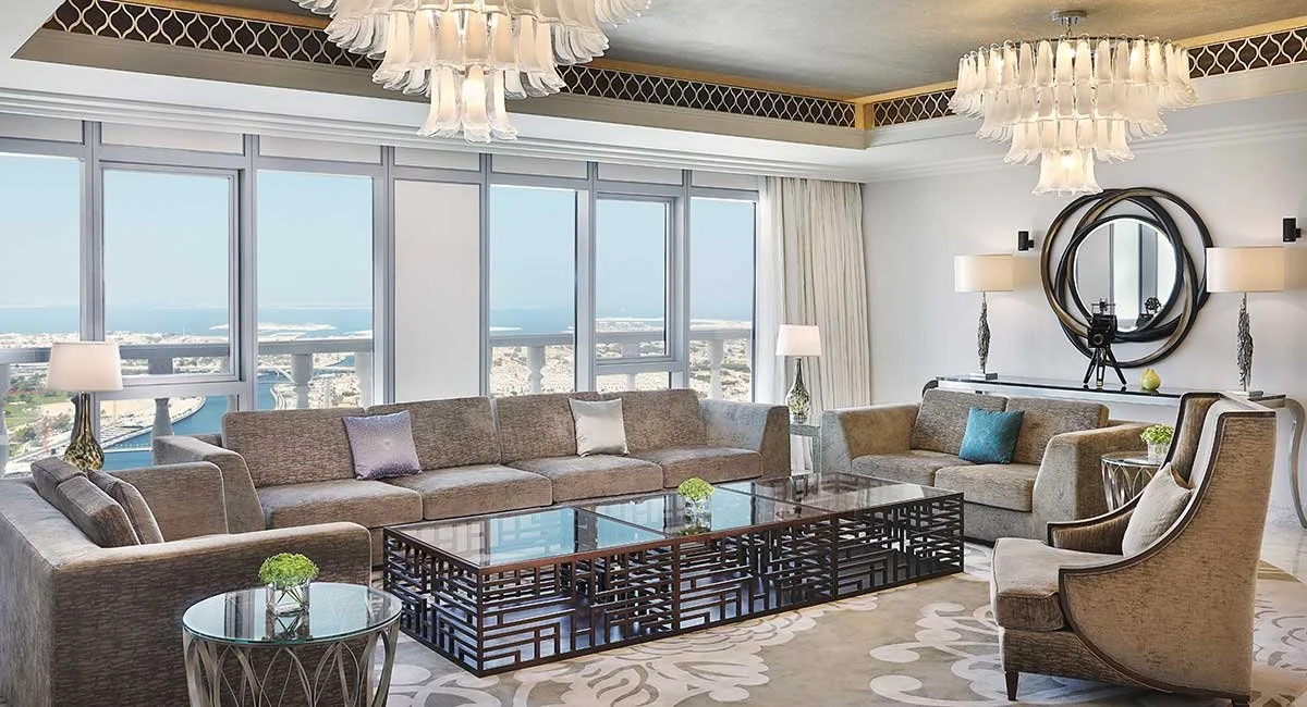 Living room with large windows, beige sofas, decorative pillows, a glass coffee table, and modern lamps, overlooking a cityscape and water view.