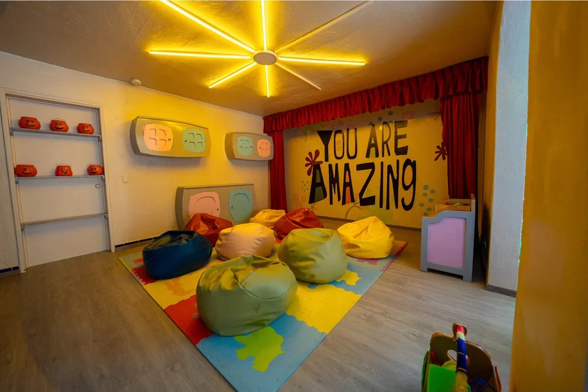 Colorful children's playroom with bean bags, a mural that says "You Are Amazing," and shelves with pumpkin-shaped decorations.