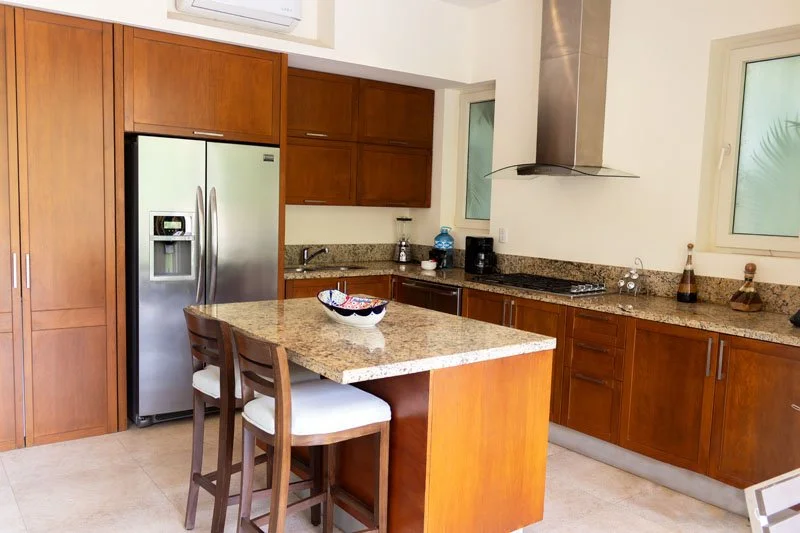 Modern kitchen with wooden cabinets, granite countertops, stainless steel refrigerator, and island with two chairs.