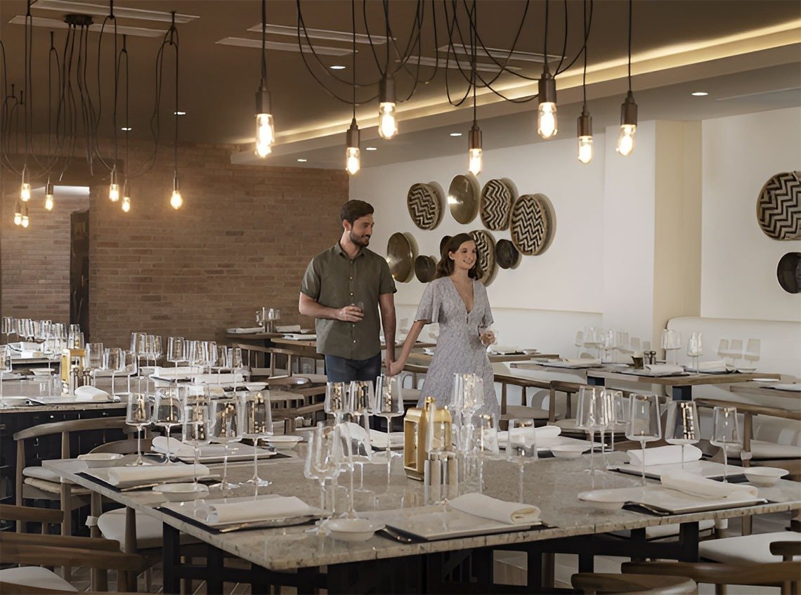 A couple in a well-lit restaurant holding hands, with empty tables set with glasses, plates, and utensils, and decorative wall art with circular patterned plates.