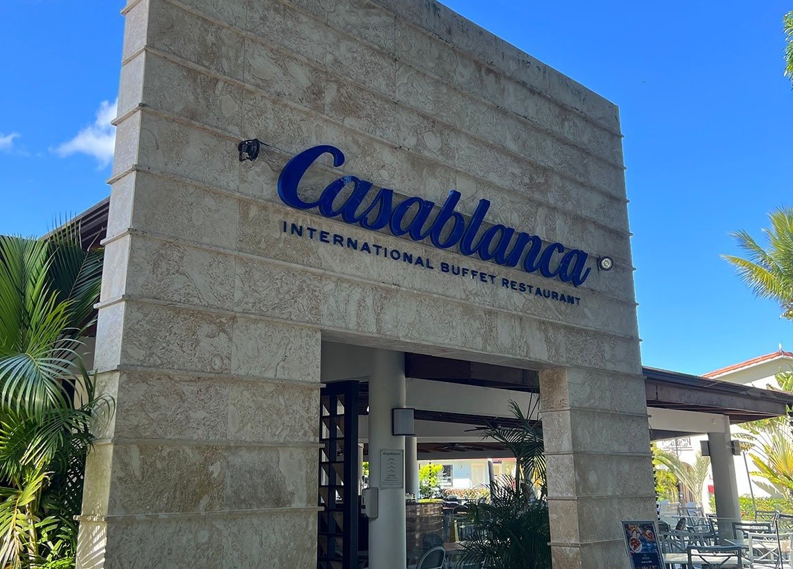 Entrance sign for Casabella International Buffet Restaurant with a stone facade and surrounding tropical plants.