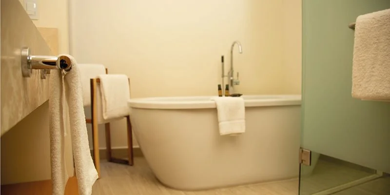 A bathroom with a bathtub, a towel hanging on a rack, a chair, and a green cabinet.