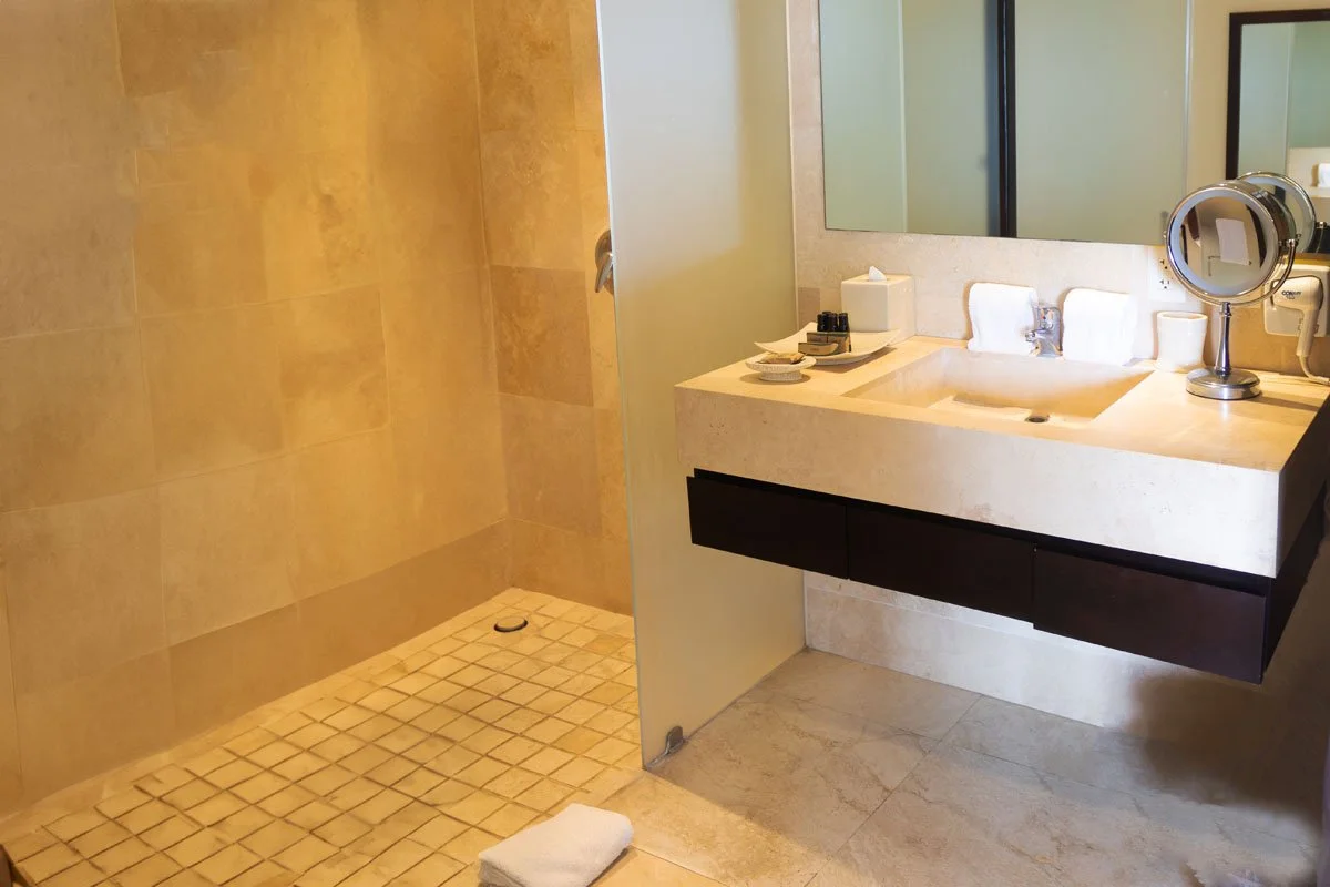 Modern bathroom with beige tiled shower area and a sink with a large mirror, soap, and toiletries.