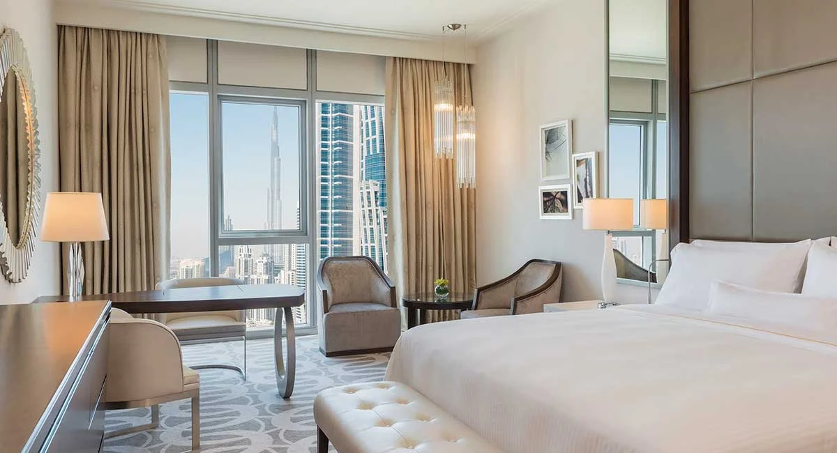 Elegant hotel room with a large bed, seating area, and city view of skyscrapers including the Burj Khalifa.