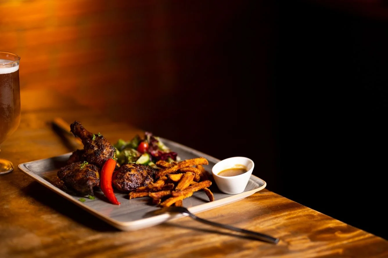 Plate with grilled chicken, French fries, salad, and dipping sauce on a wooden table.
