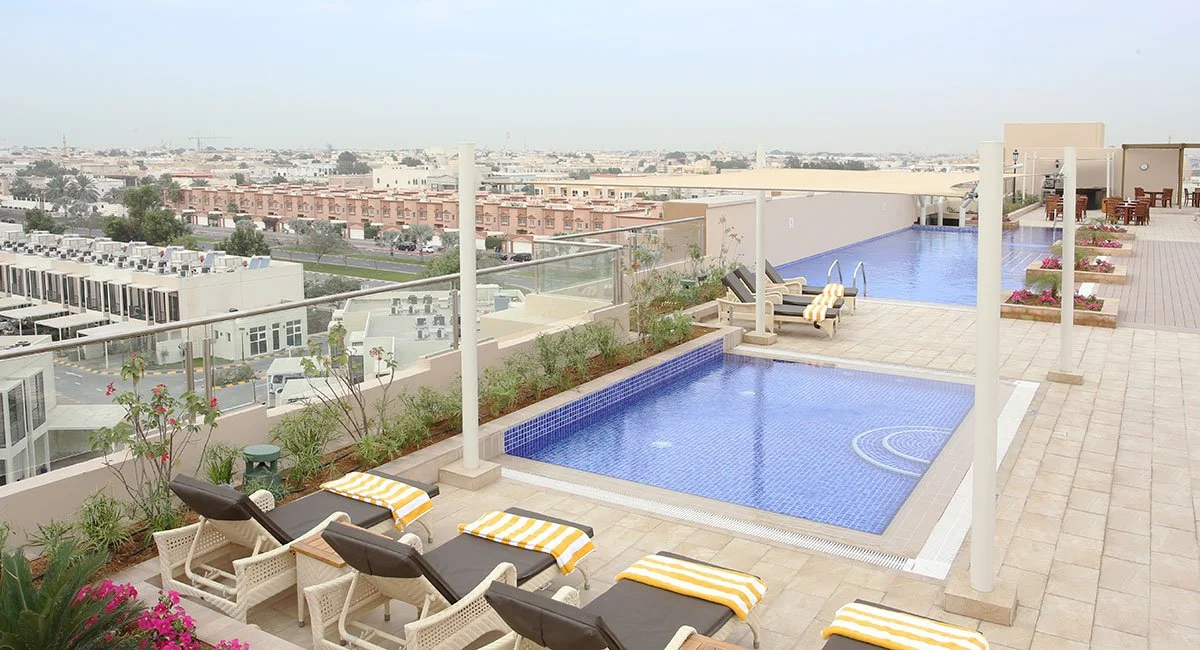 Rooftop swimming pool with lounge chairs, striped towels, and city view in the background.