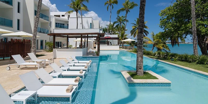 Pool area at a beachfront resort with lounge chairs, palm trees, and ocean views.
