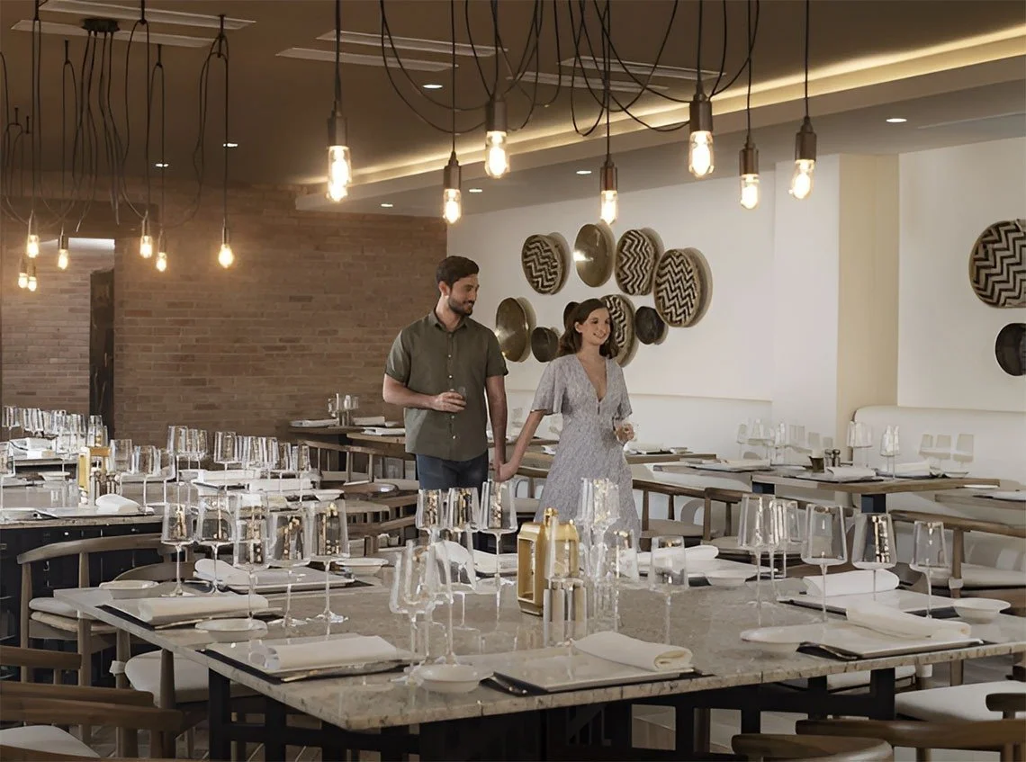 A couple holding hands inside a restaurant with modern decor, multiple tables set with glassware, napkins, and cutlery, and pendant lights hanging from the ceiling.