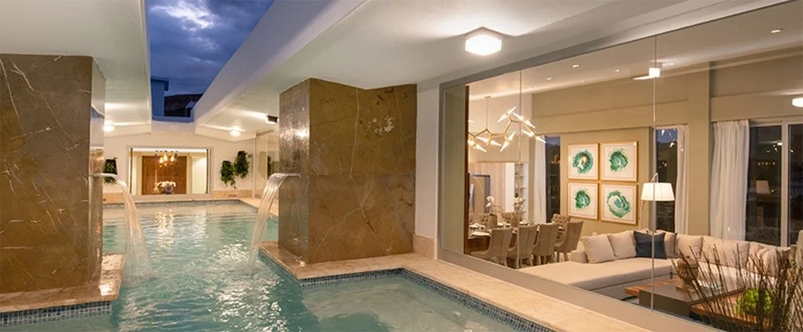 Indoor swimming pool area with water features and a view into a modern living and dining room.