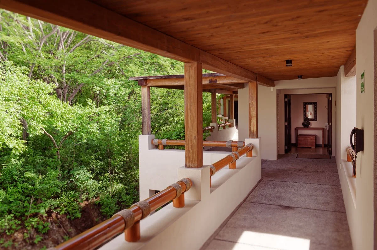 Balcony with wooden railing and ceiling, overlooking green, leafy trees outside.