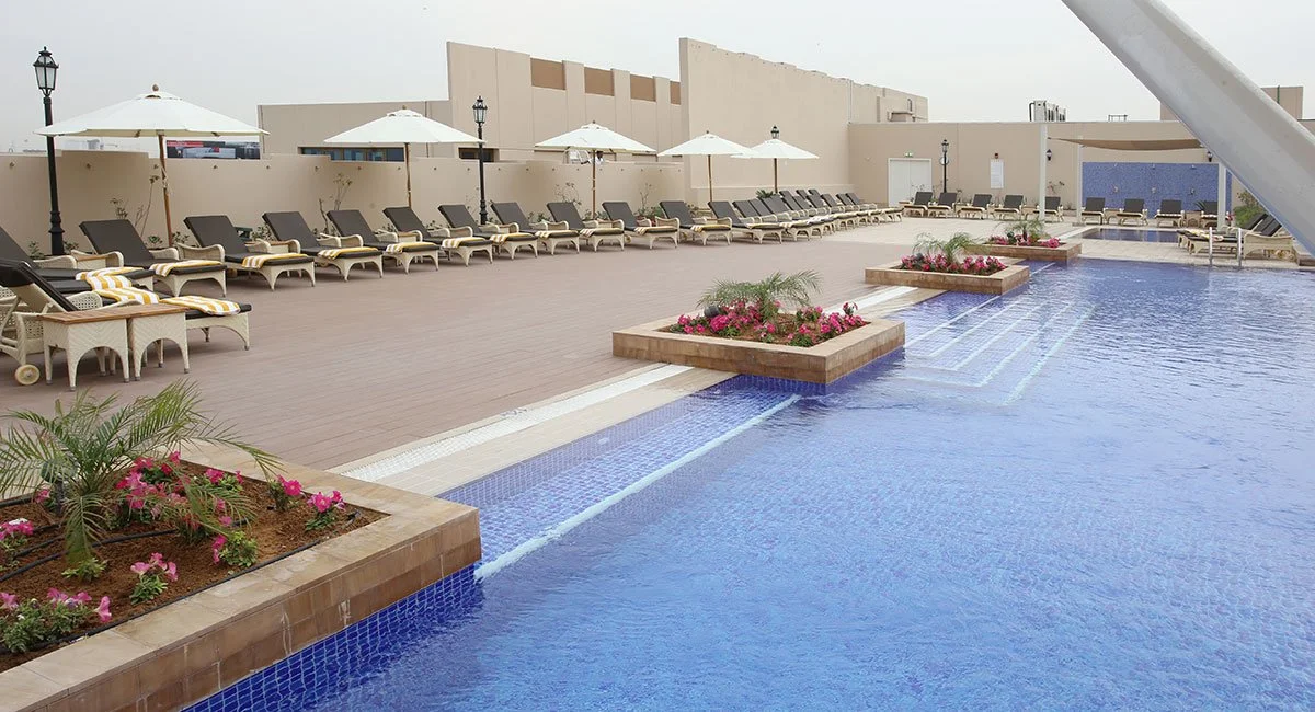 Hotel rooftop pool with lounge chairs, umbrellas, and flower planters.