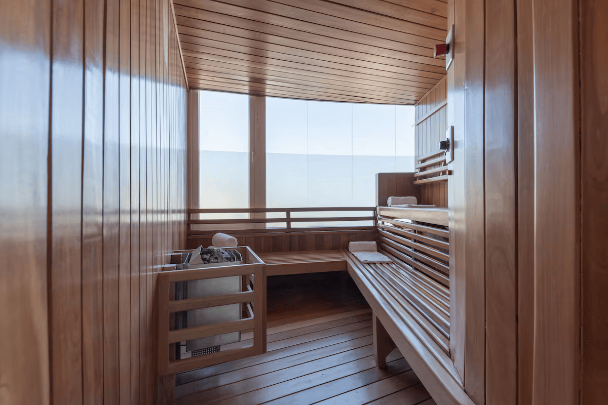 A wood-paneled interior of a sauna with benches, towels, and a heater with stones.