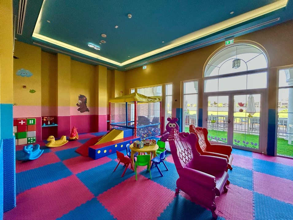 Colorful children's playroom with slide, soft seating, small table with chairs, and large windows letting in natural light.