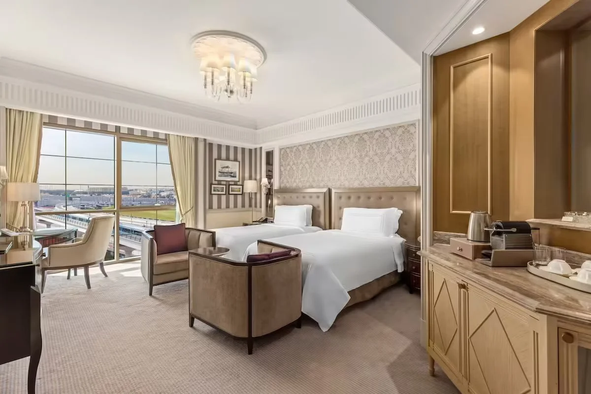 Hotel room with two beds, a window view, seating area, and a nightstand.