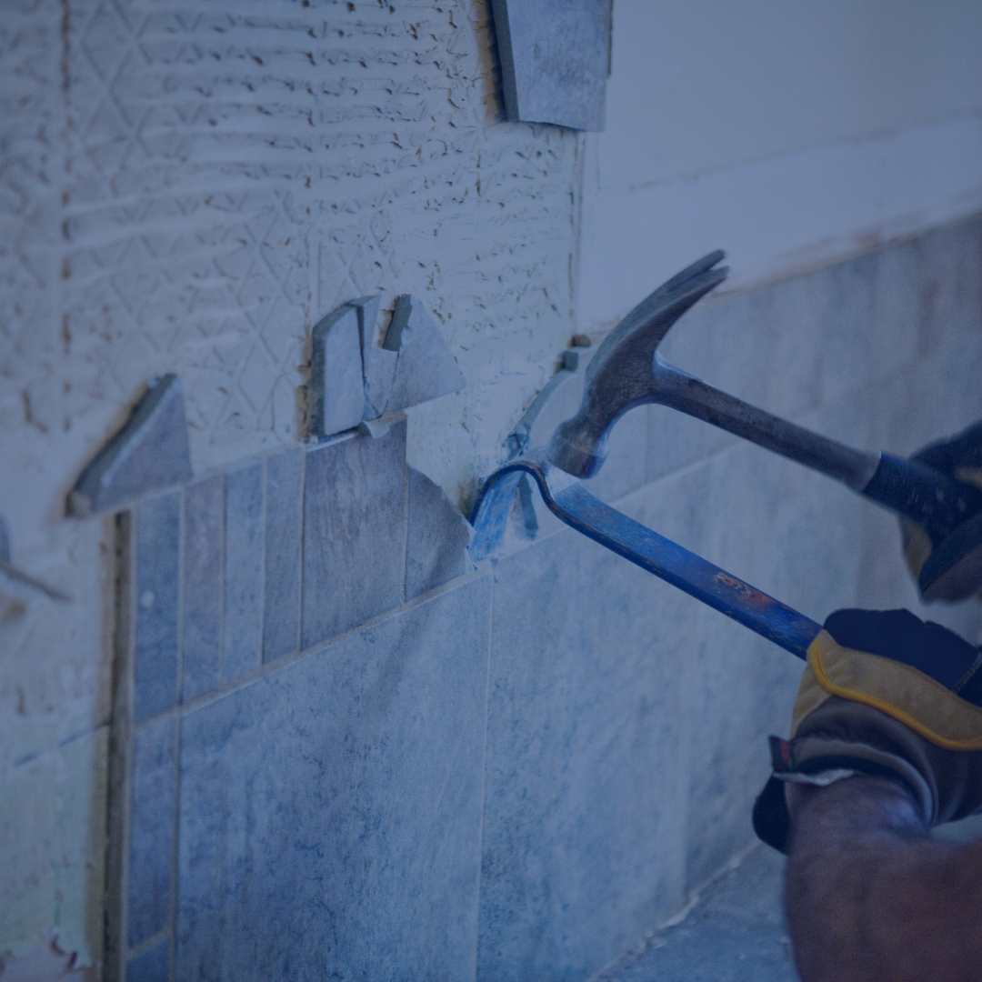 A person using a hammer and chisel to remove tiles from a wall during tile removal work.
