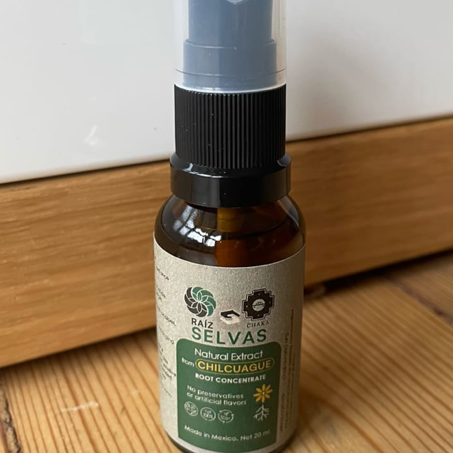 A small brown spray bottle with a black spray nozzle, labeled as Raiz Selvas natural extract from Chilicauque, Mexico, containing 20 ml. The bottle is placed on a wooden surface.